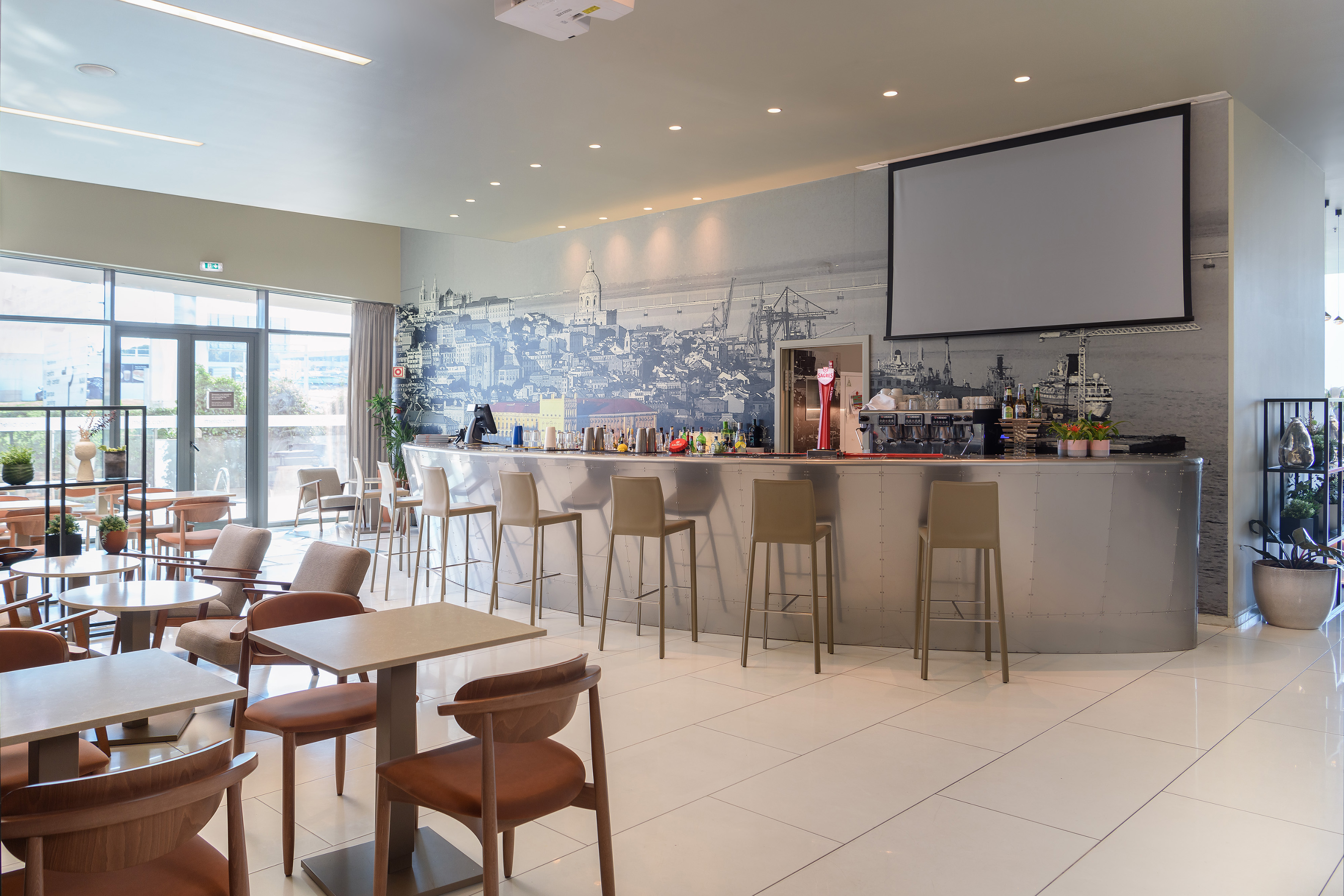 Modern hotel lounge bar with city skyline mural, projector screen, and seating.