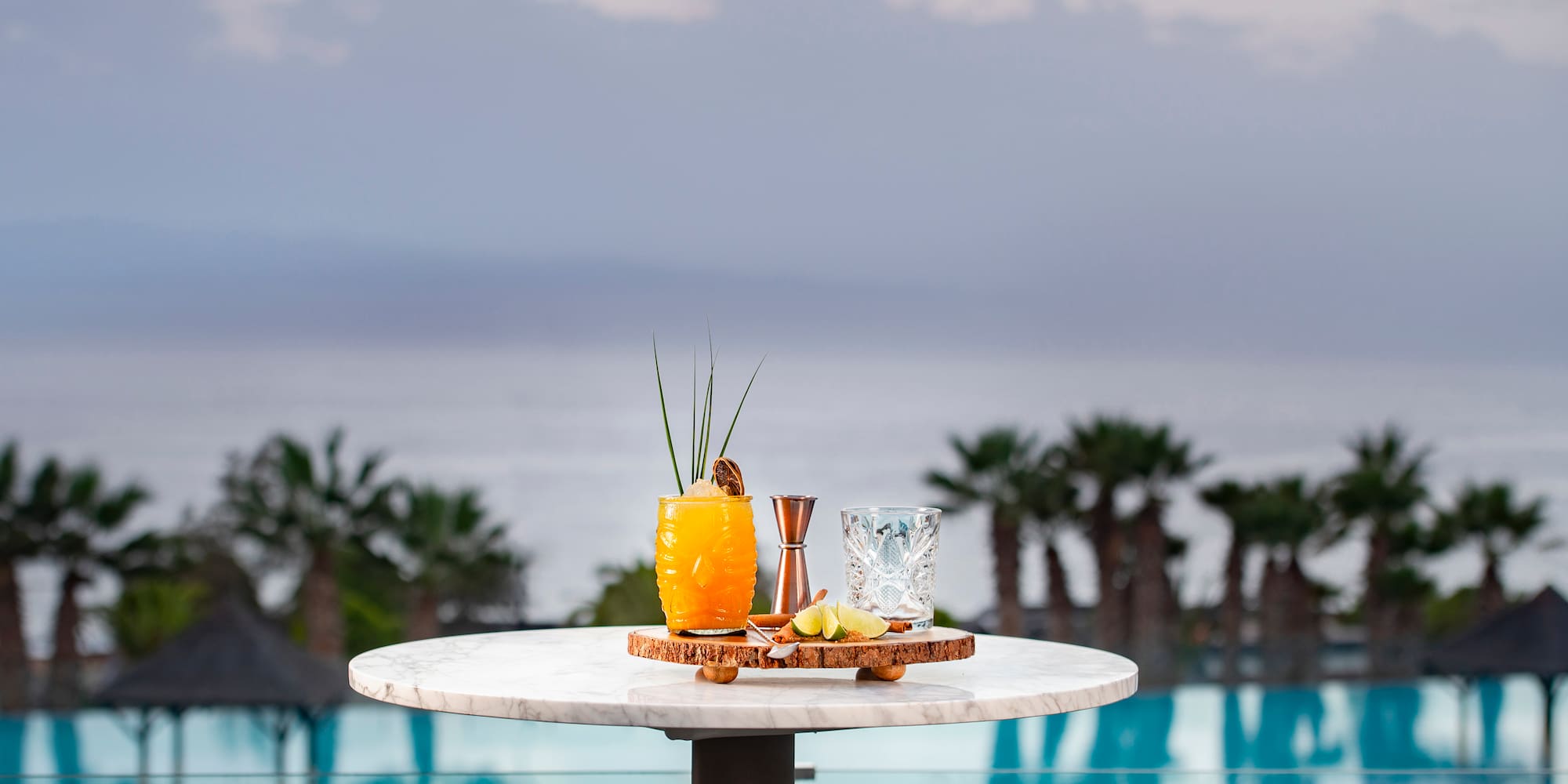 Tropical orange cocktail on marble table overlooking luxury resort pool and ocean.