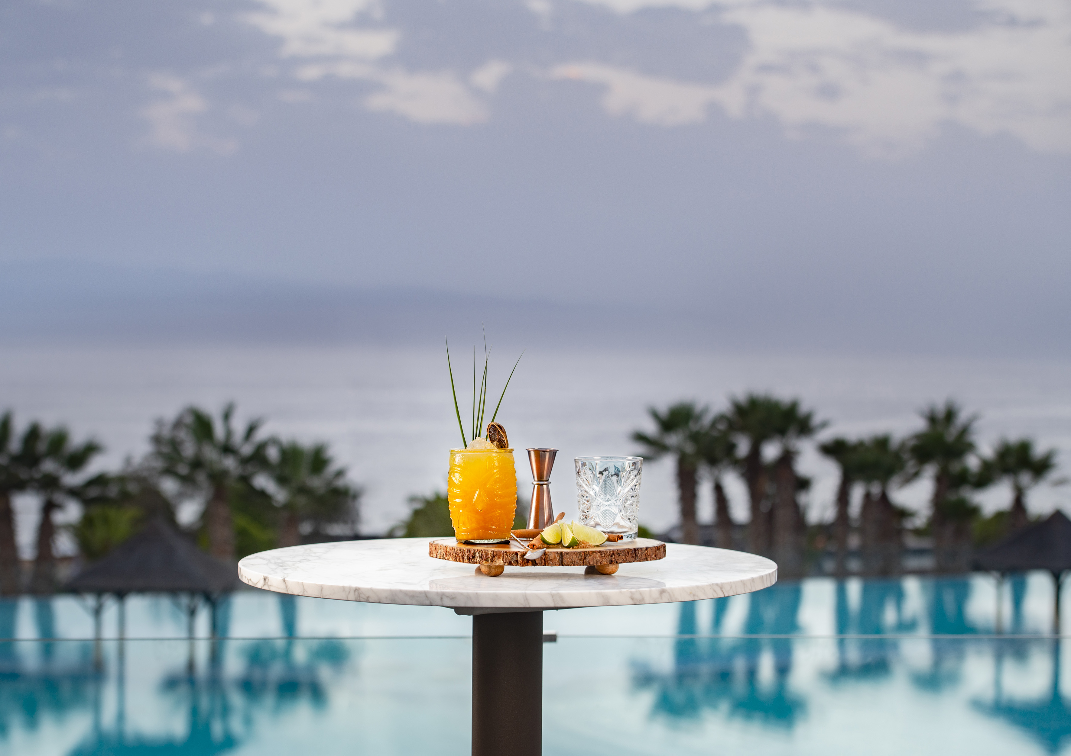 Tropical orange cocktail on marble table overlooking luxury resort pool and ocean.