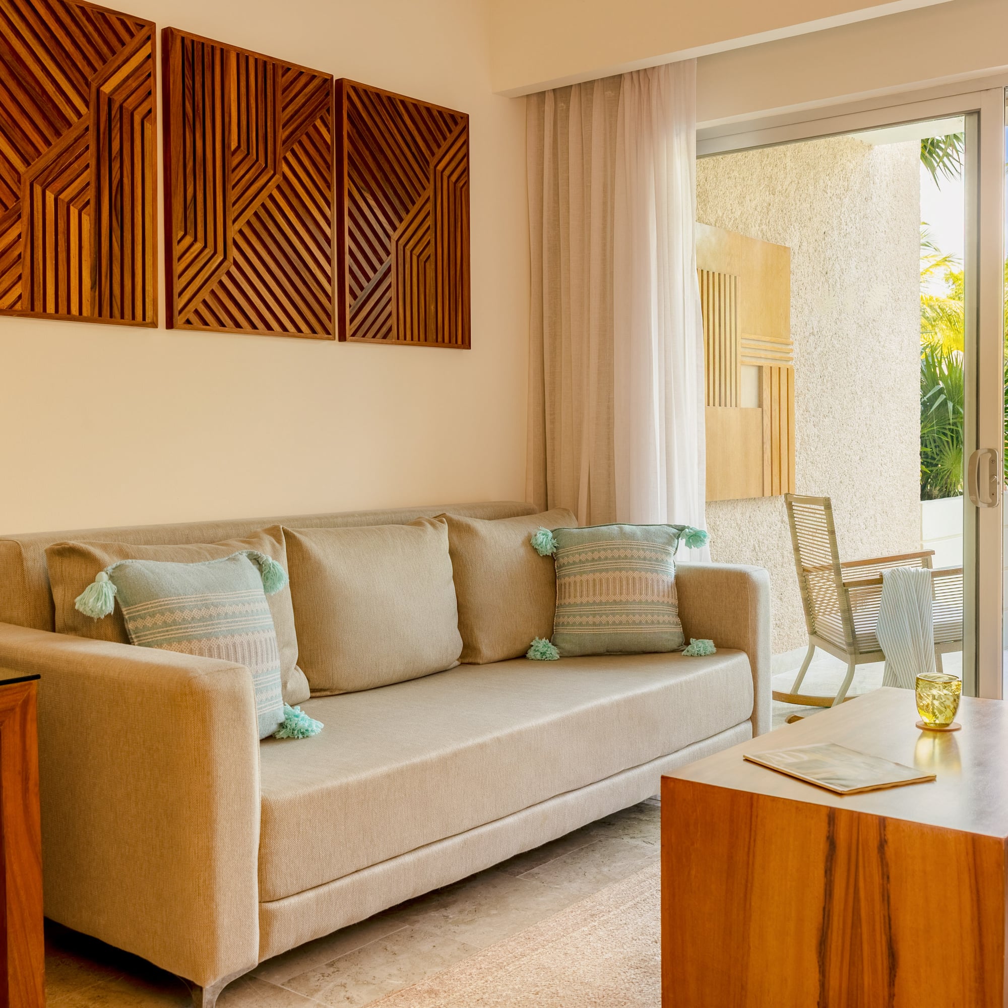 Tropical resort living room with beige sofa, wooden art, and patio pool view.