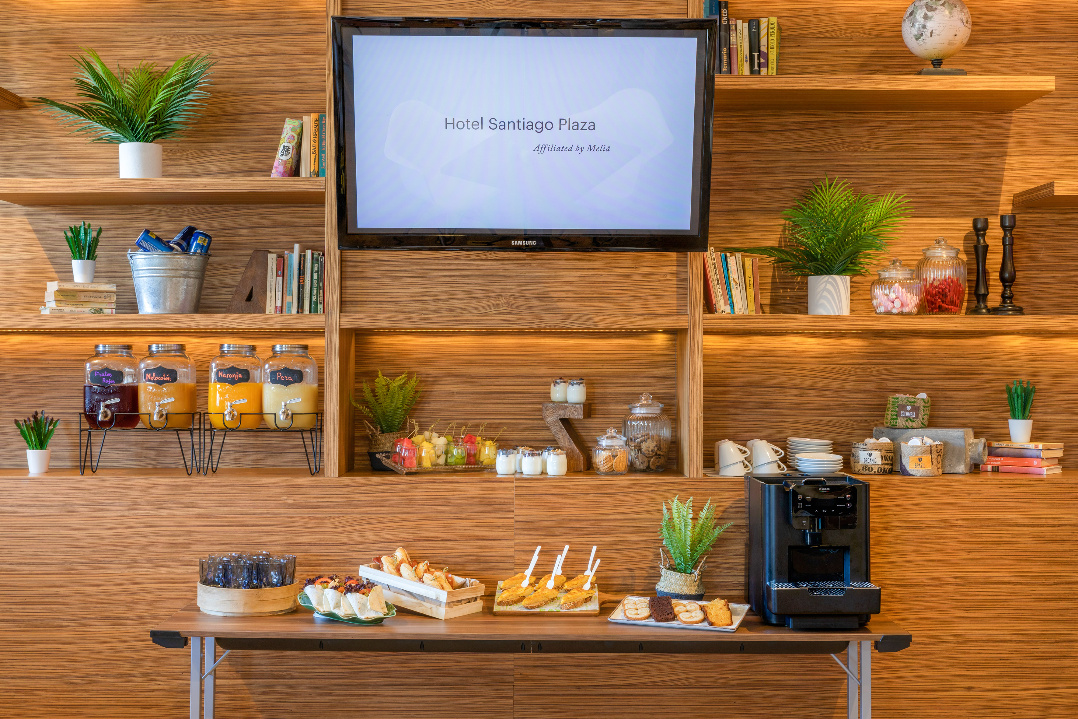 Hotel Santiago Plaza lobby buffet: juices, snacks, coffee machine, welcome screen.