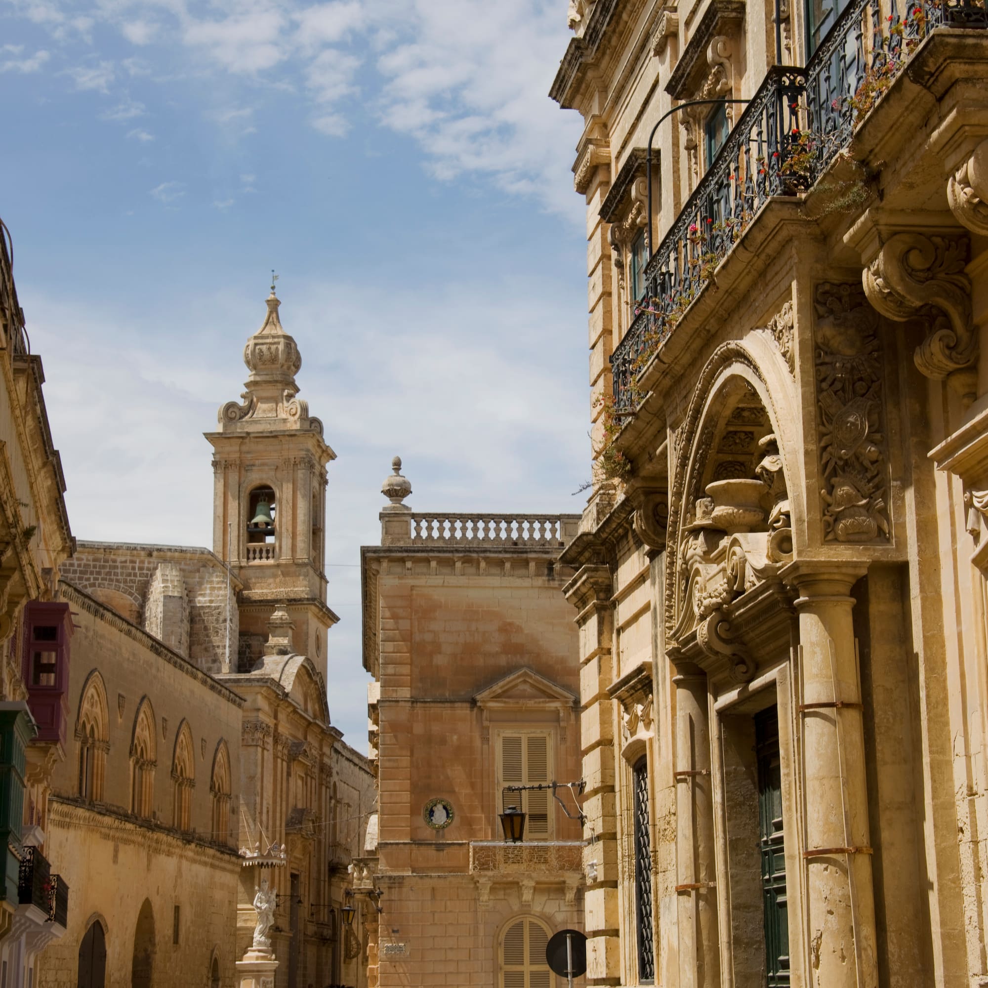 Historic Mdina street with ornate limestone buildings and prominent bell tower.