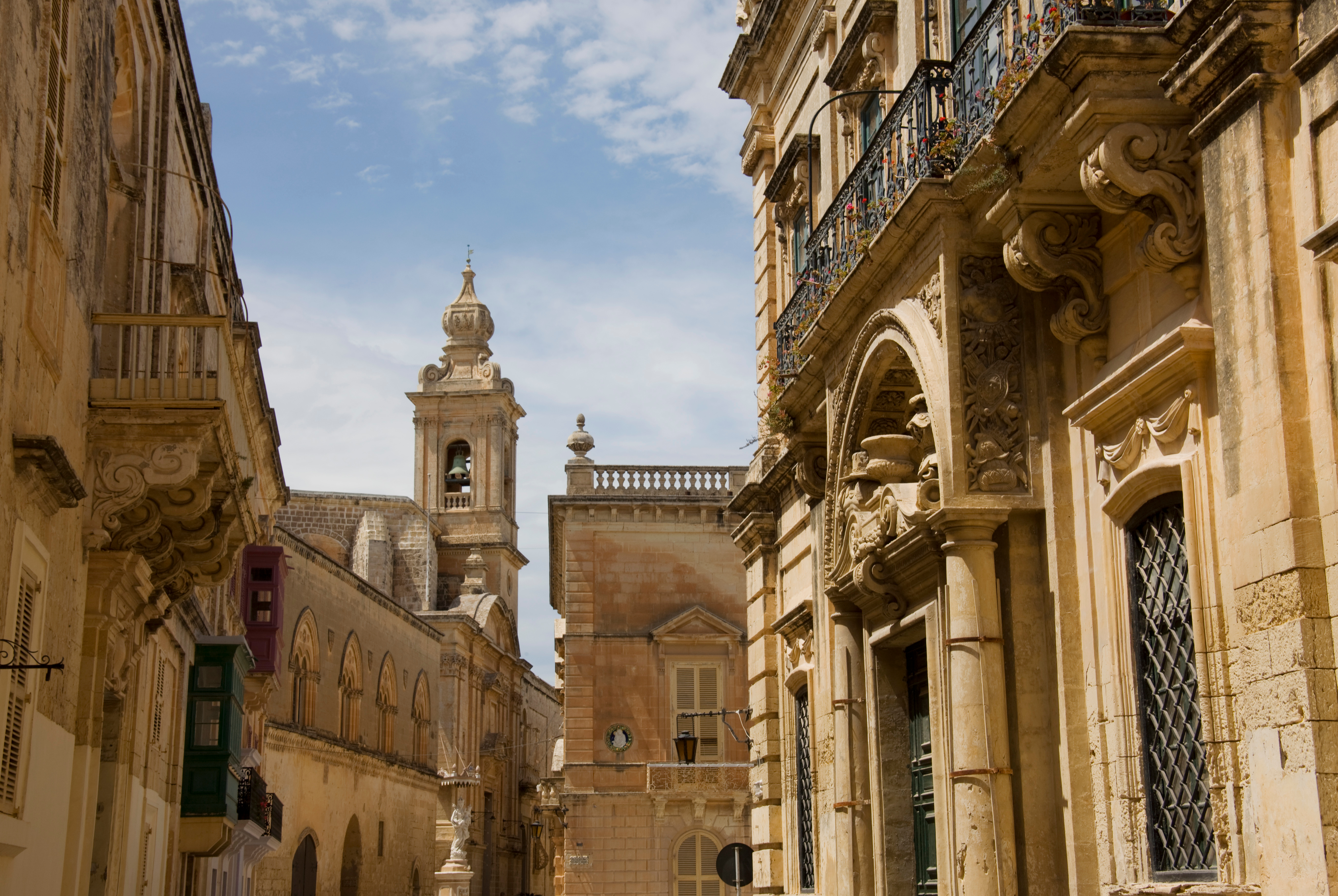 Historic Mdina street with ornate limestone buildings and prominent bell tower.
