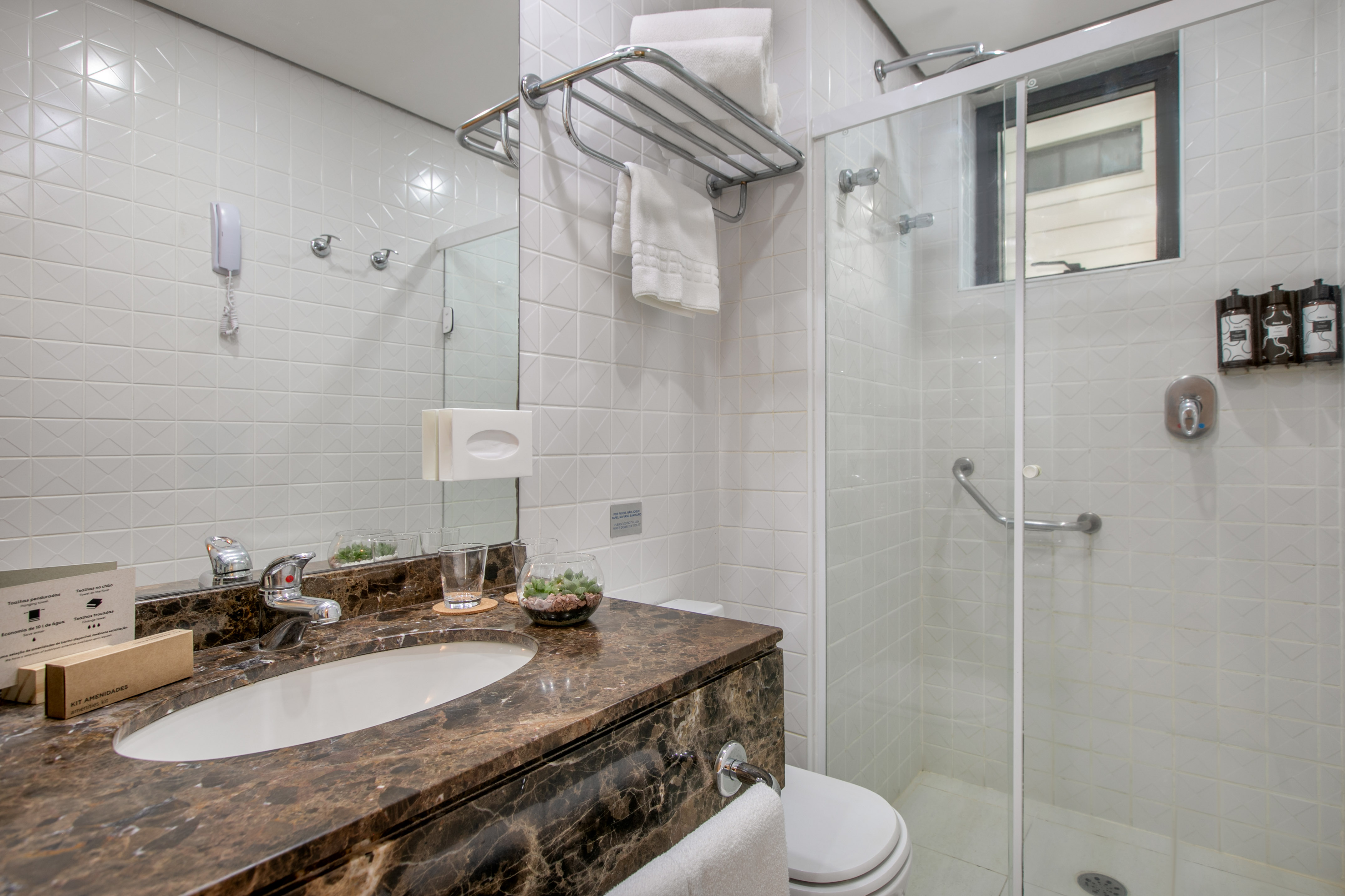 Accessible hotel bathroom with white tiles, marble vanity, sink, and glass shower.