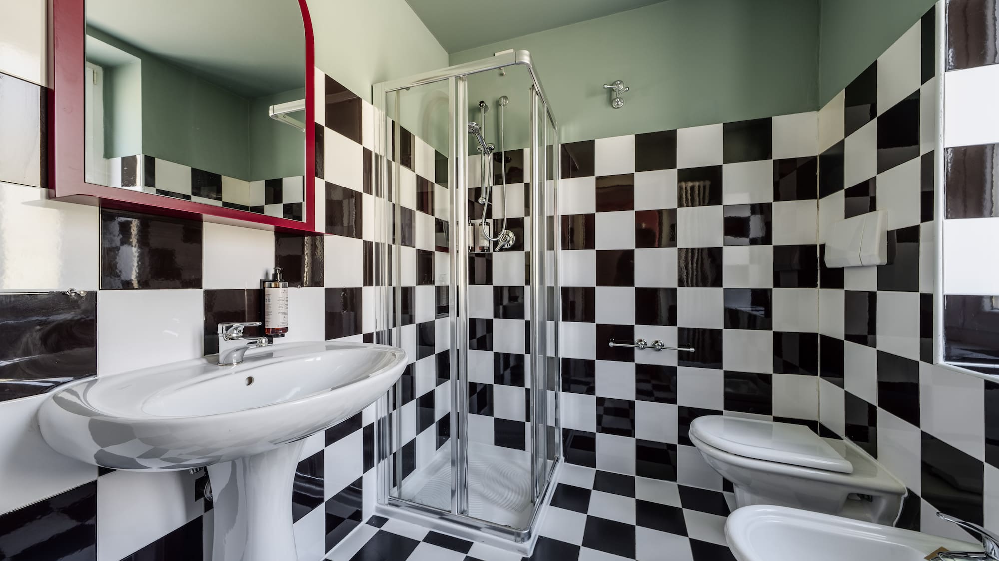 Black and white checkered tile bathroom with shower, sink, toilet, and bidet.
