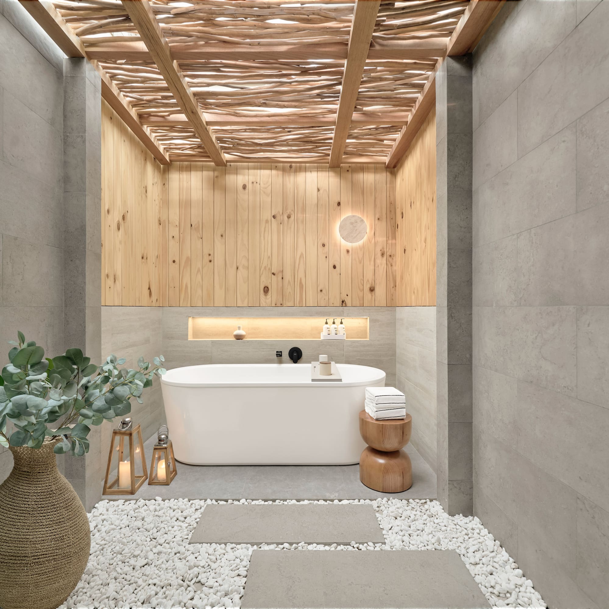 Spa bathroom with freestanding tub, wood ceiling, stone walls, pebble floor.