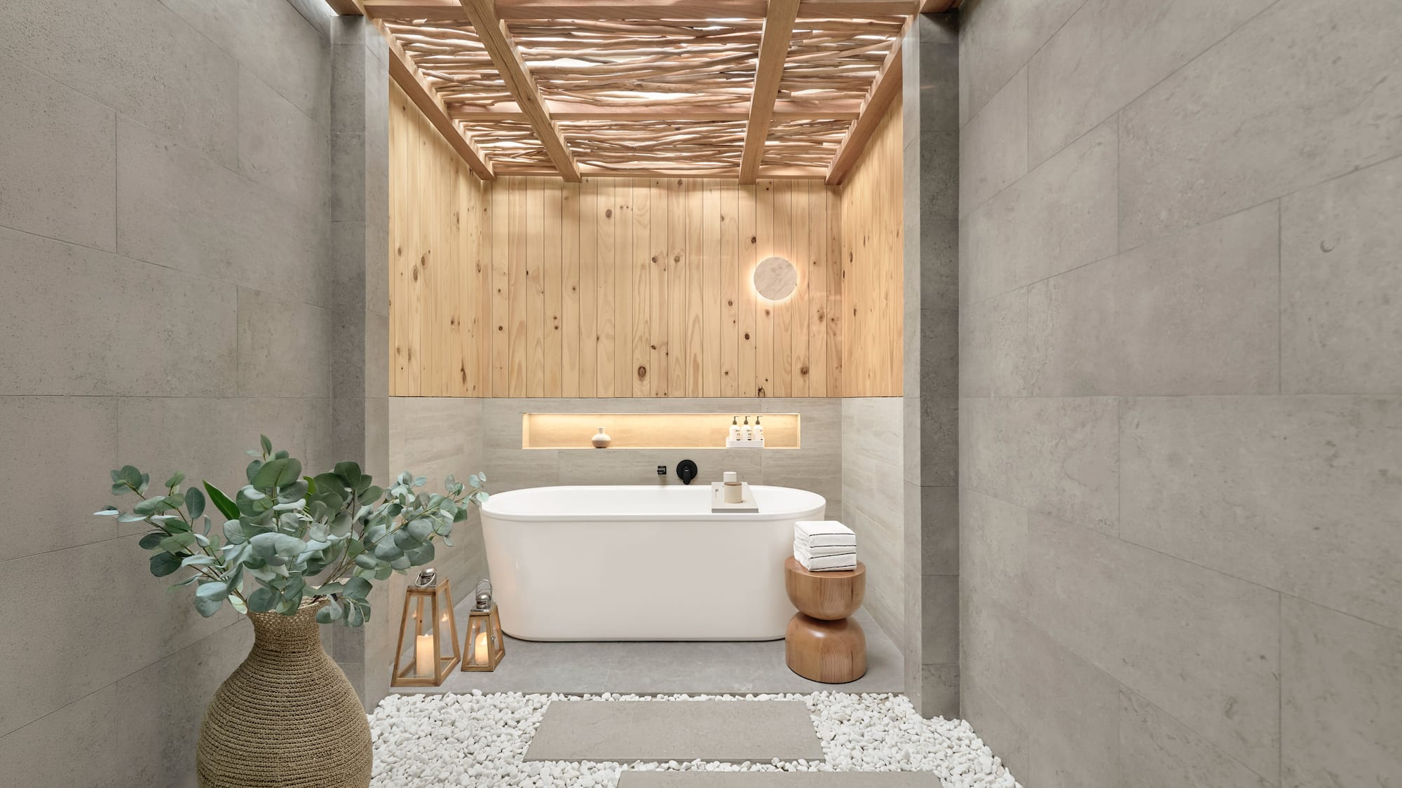Spa bathroom with freestanding tub, wood ceiling, stone walls, pebble floor.