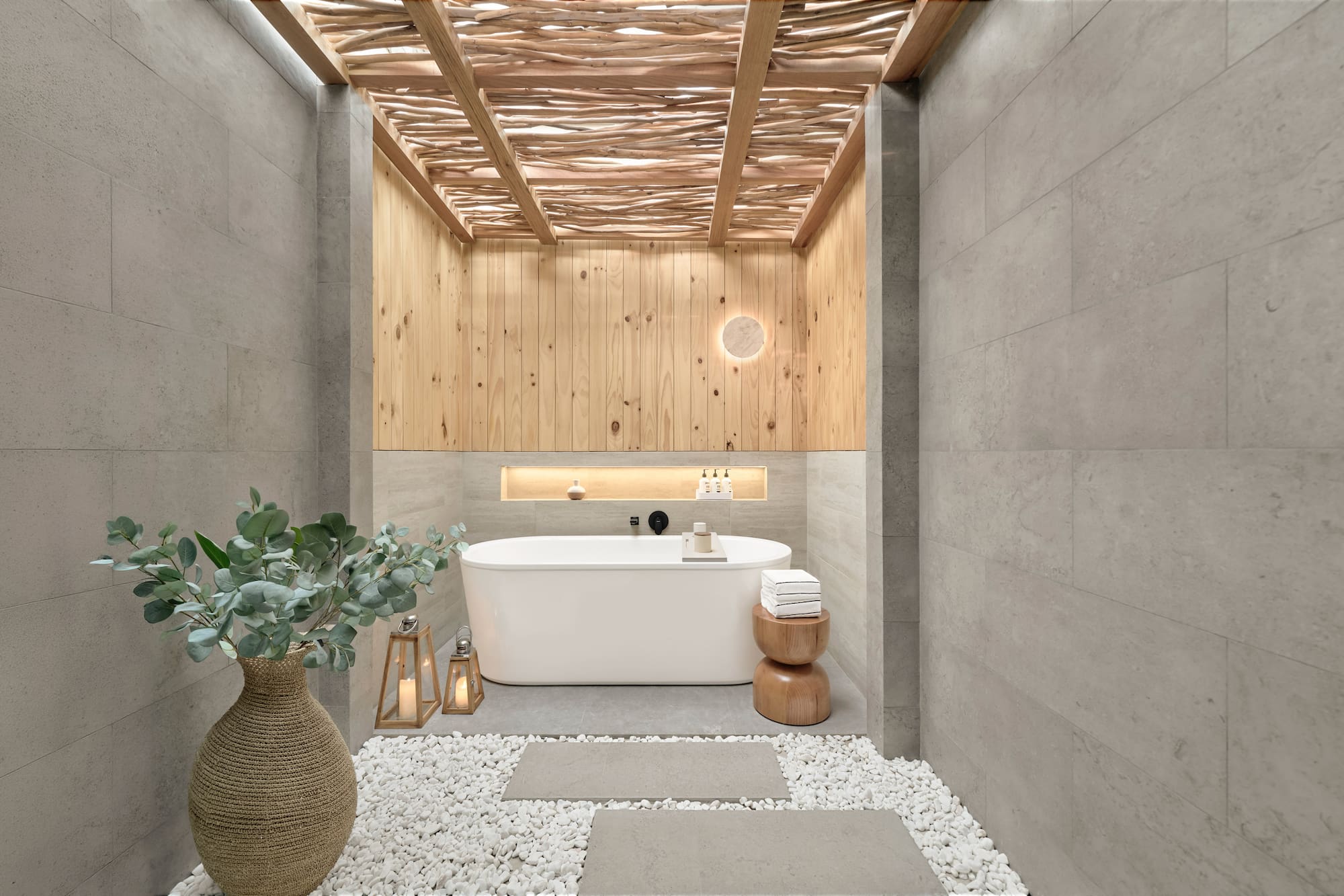 Spa bathroom with freestanding tub, wood ceiling, stone walls, pebble floor.