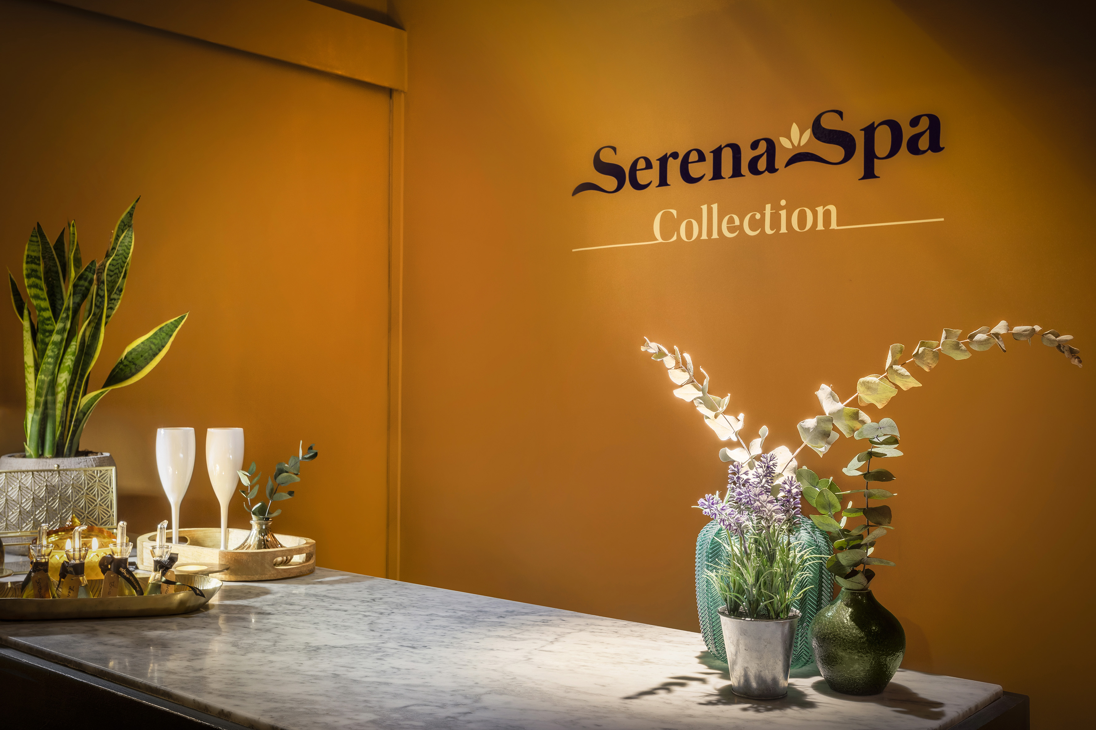 Serena Spa Collection sign above counter with spa plants, oils, and flutes.