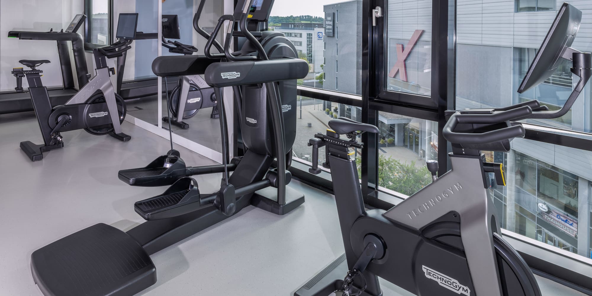 Modern hotel gym with Technogym treadmill, elliptical, and stationary bike. - Khu vực tập thể dục - INNSiDE Wolfsburg, Wolfsburg