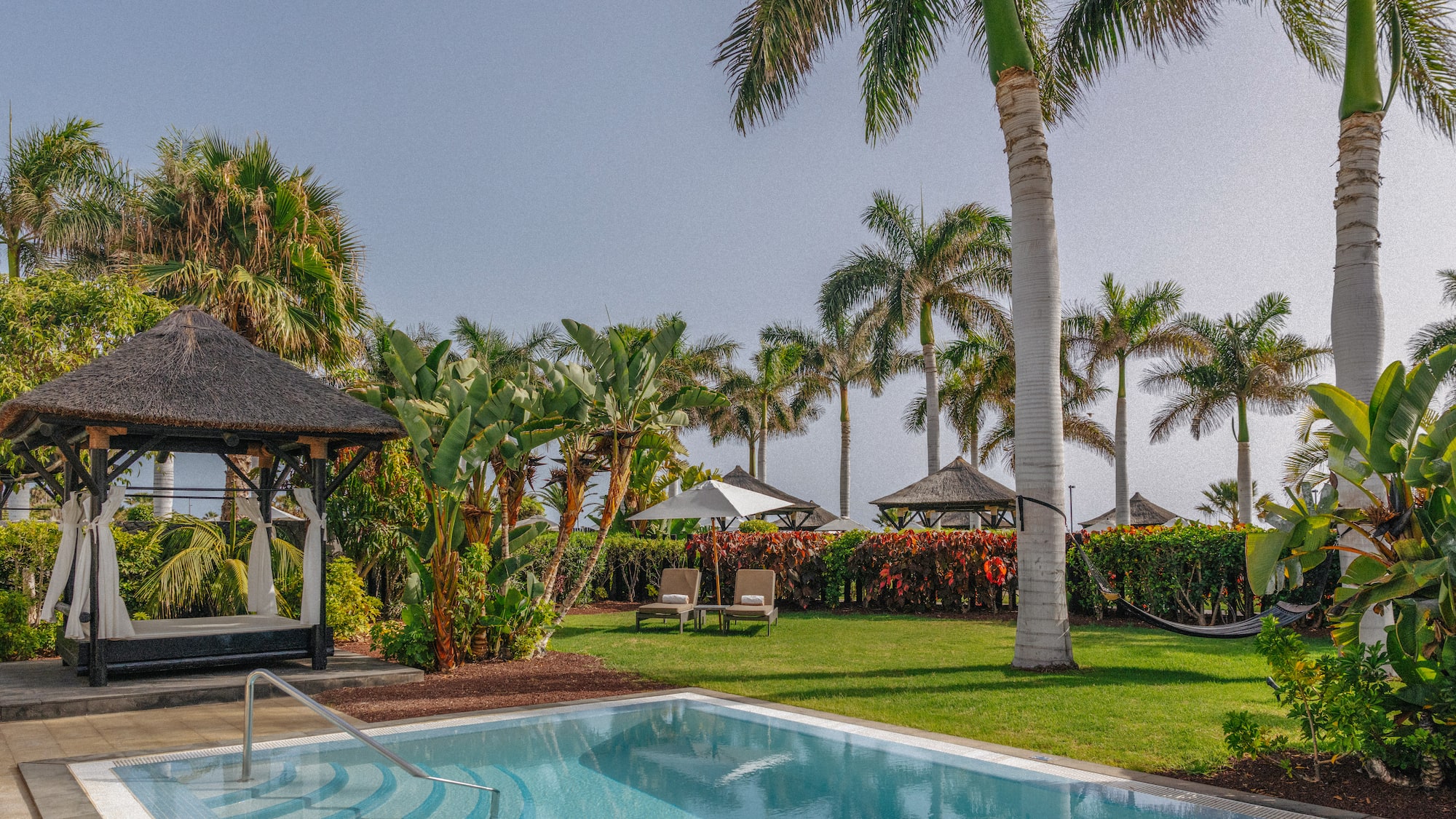 Luxury hotel private pool with tropical garden, palm trees, and thatched gazebo daybed.