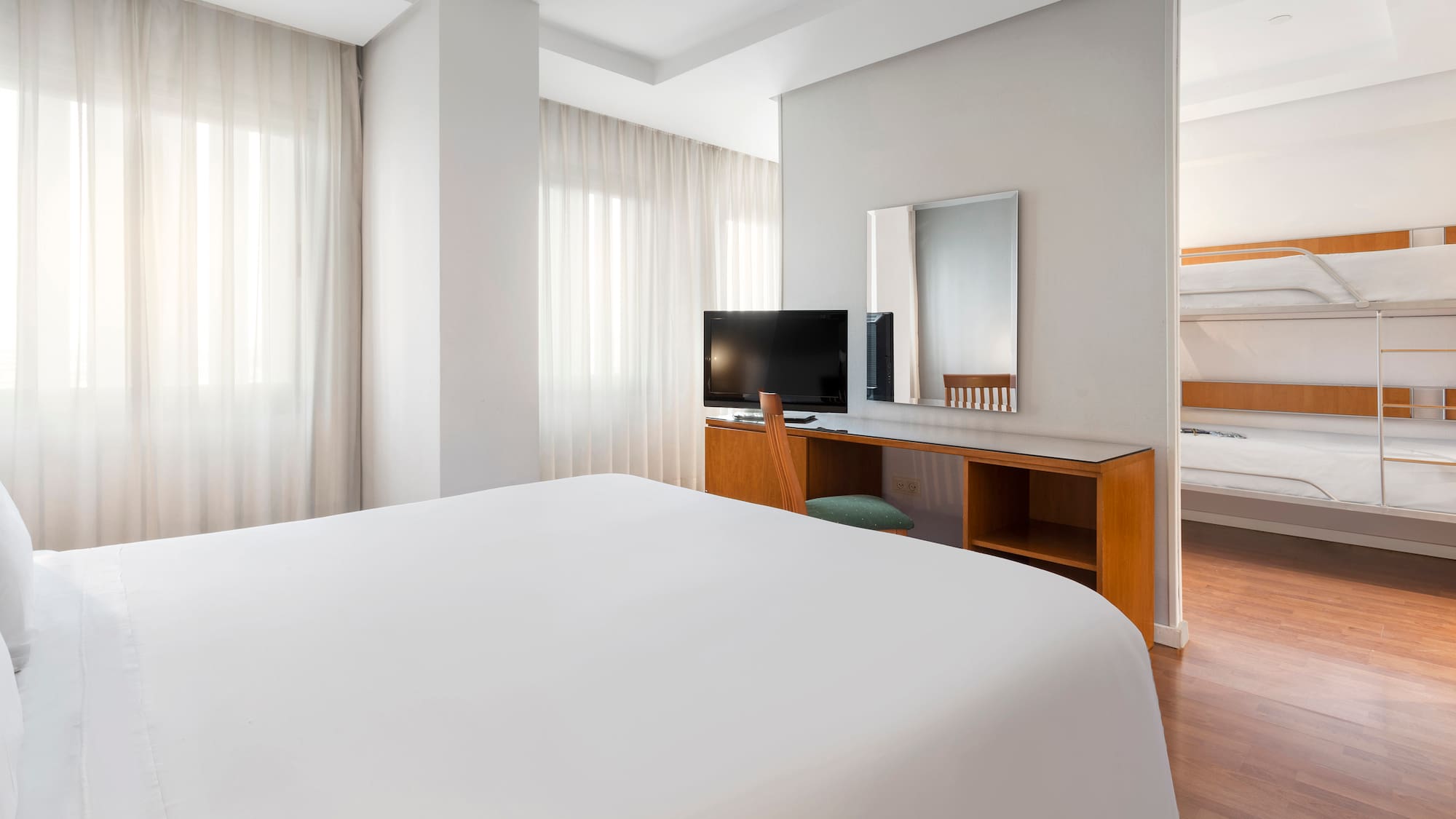 Hotel family room with queen bed, desk, TV, and adjoining bunk beds.