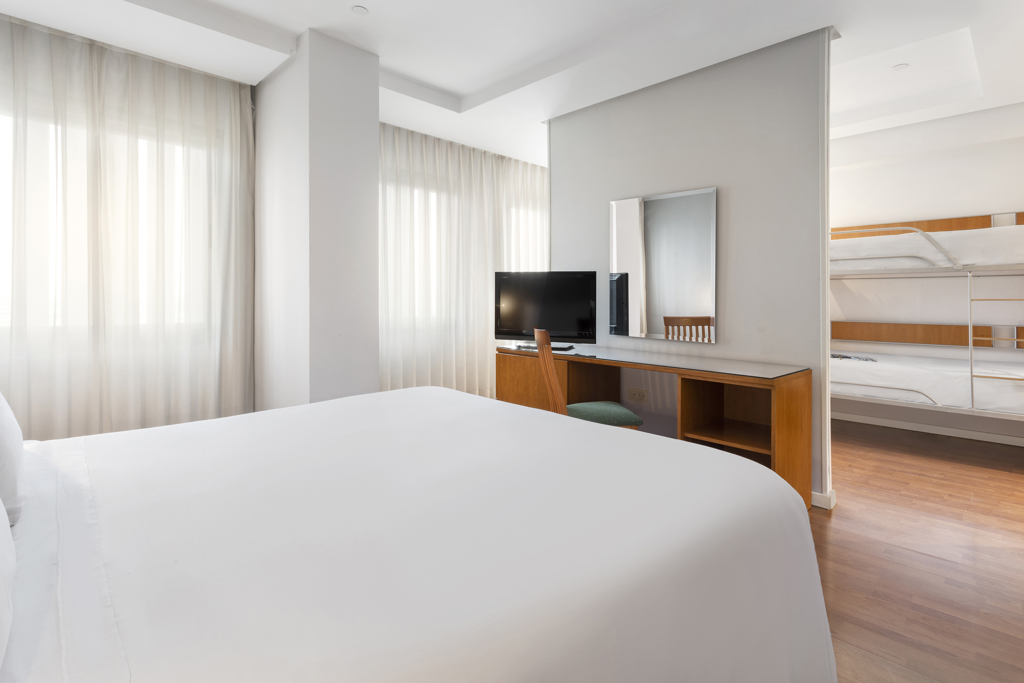 Hotel family room with queen bed, desk, TV, and adjoining bunk beds.