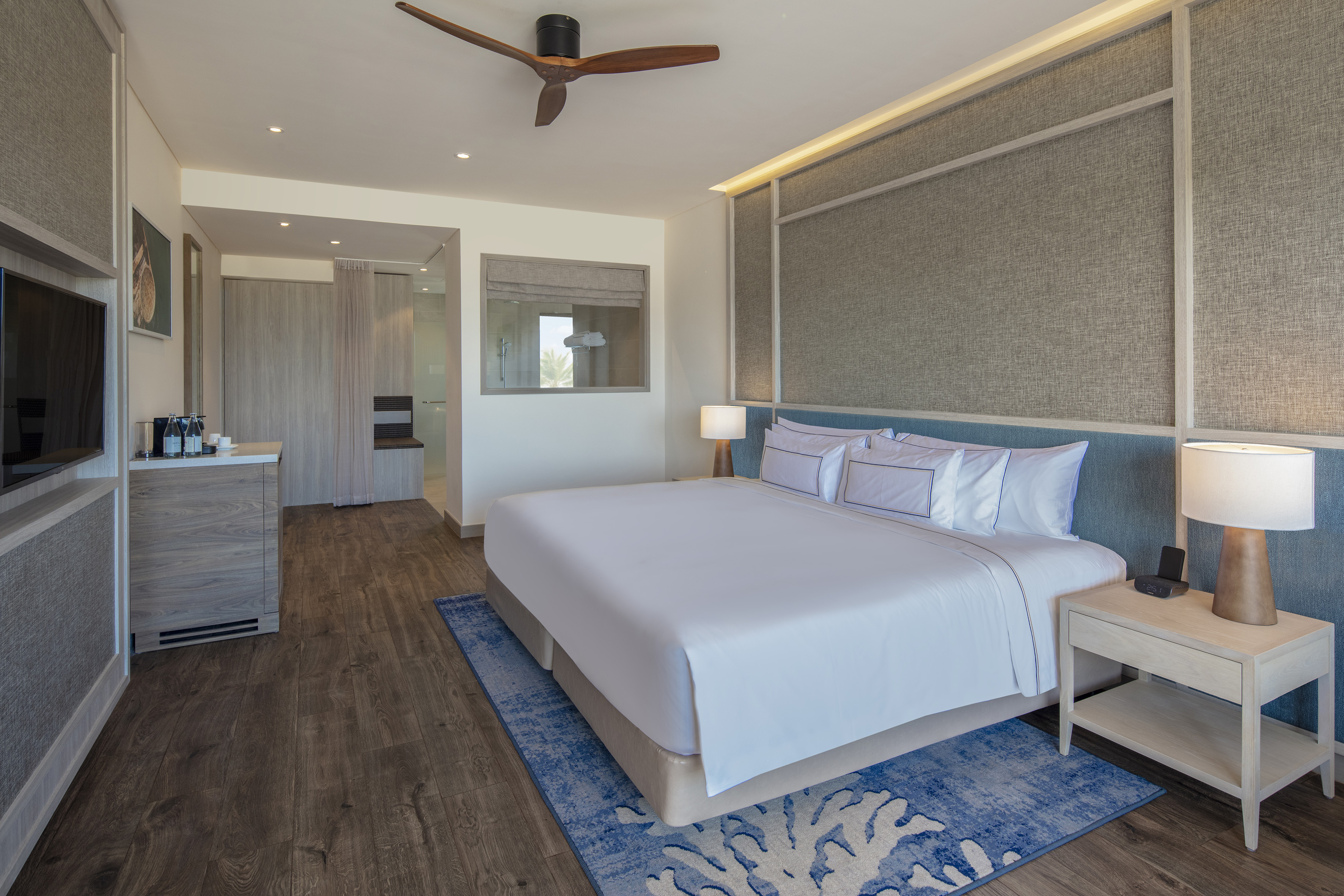 Elegant hotel bedroom with king bed, wood floor, blue coral rug, modern design.