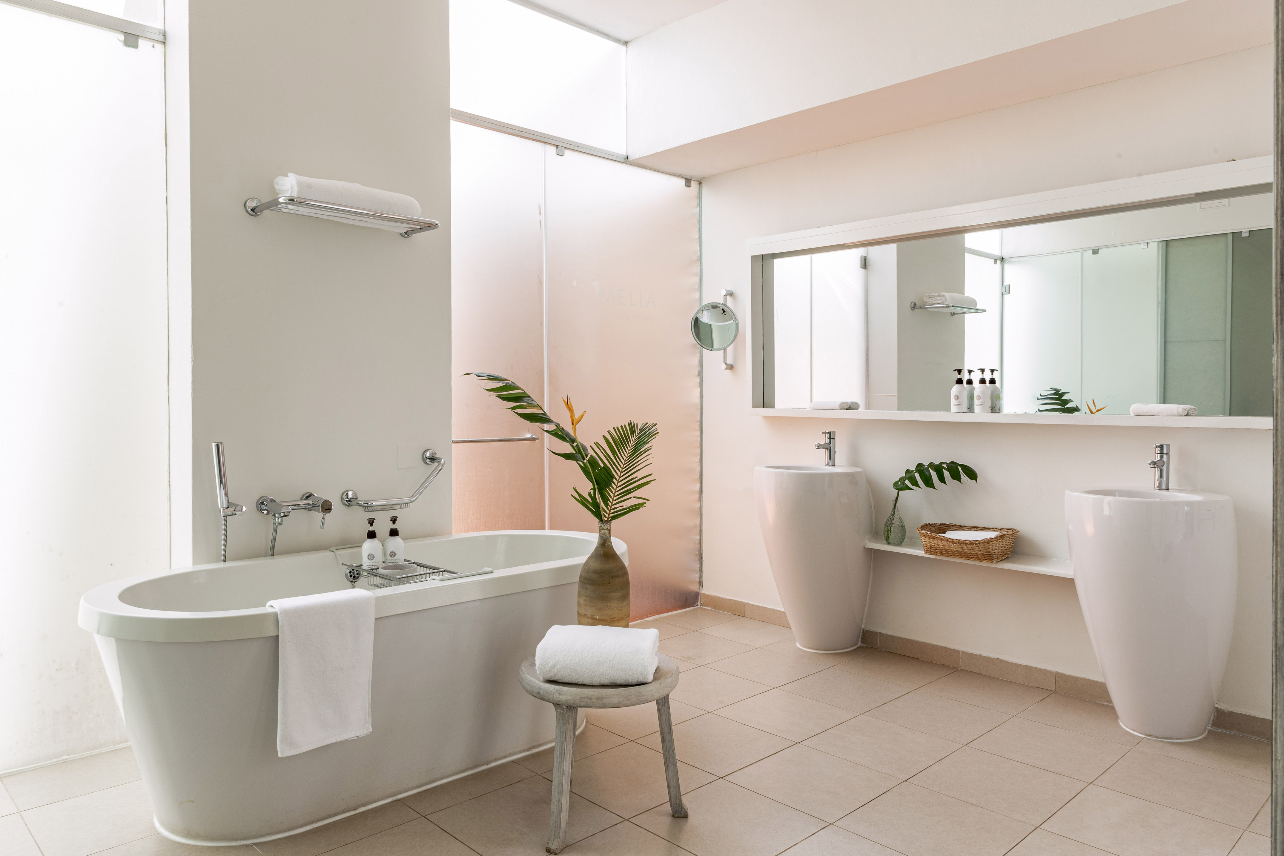 Modern white Melia bathroom with tub, dual sinks, and glass shower.