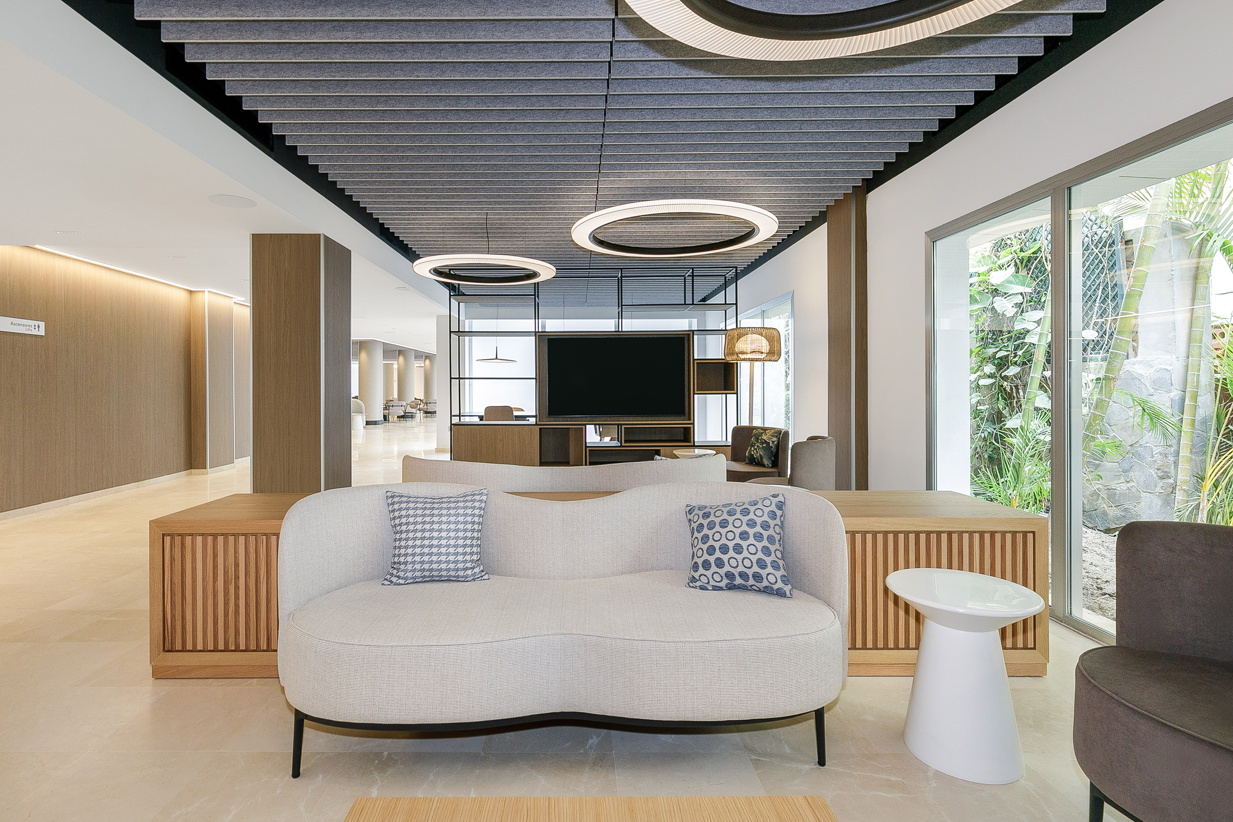 Modern hotel lobby lounge with curved sofa, acoustic ceiling, and garden view.