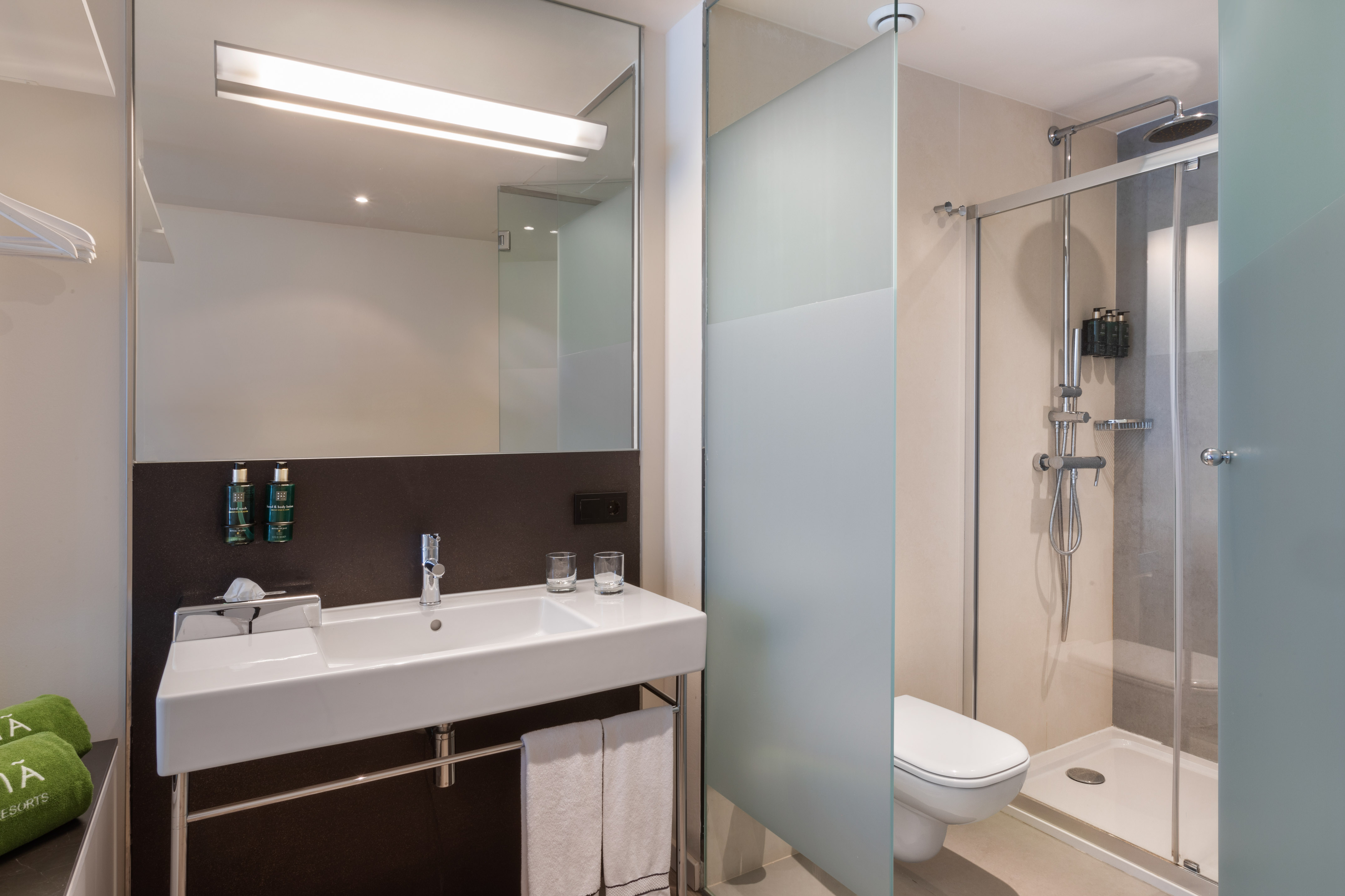 Modern hotel bathroom with white sink, large mirror, glass shower, and toilet.