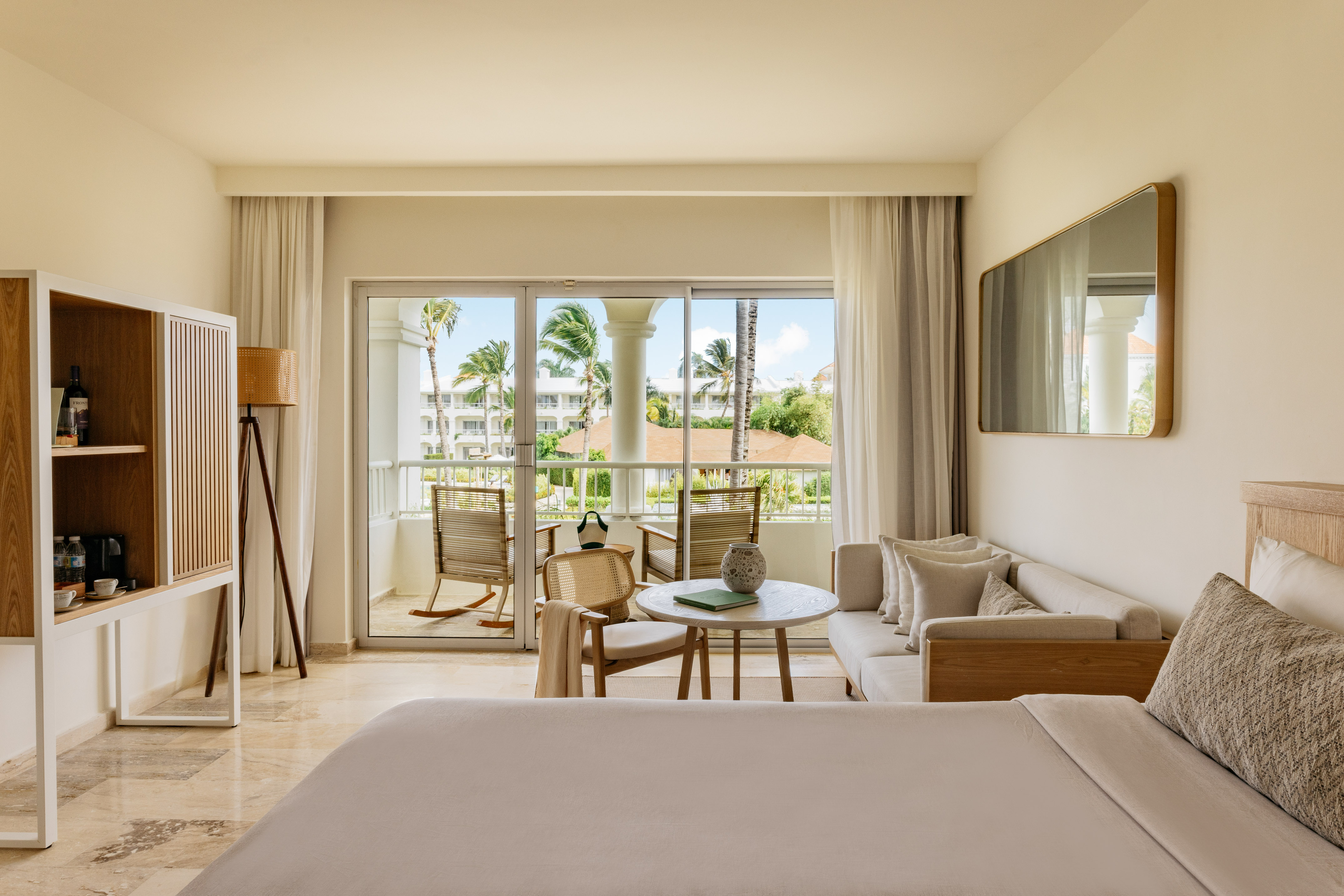 Hotel suite with private balcony, tropical palm trees, and modern decor.