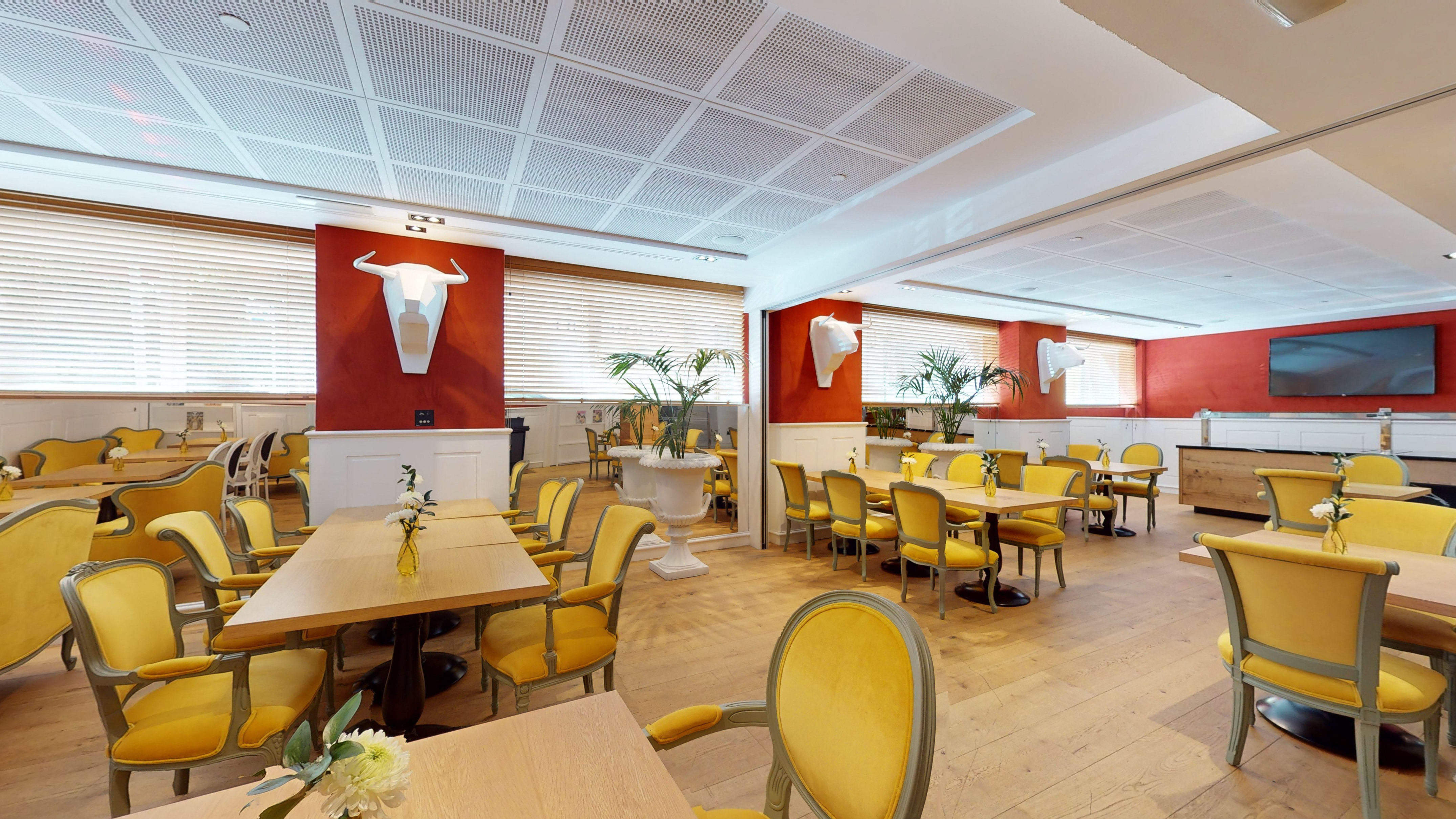 Restaurant interior: yellow chairs, wooden tables, red walls, geometric bull decor.