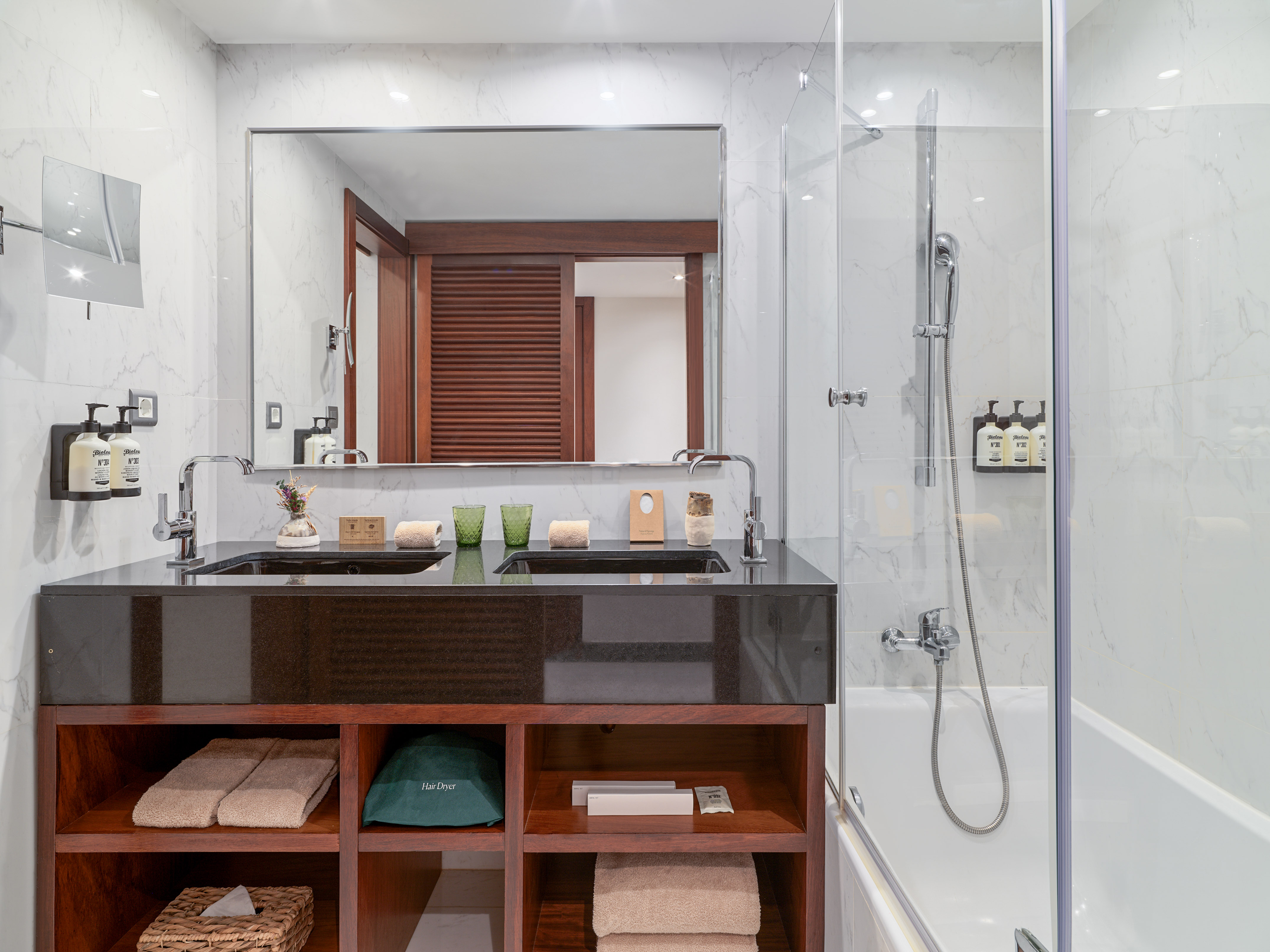 Modern hotel bathroom with marble, black double vanity, shower, and bathtub.