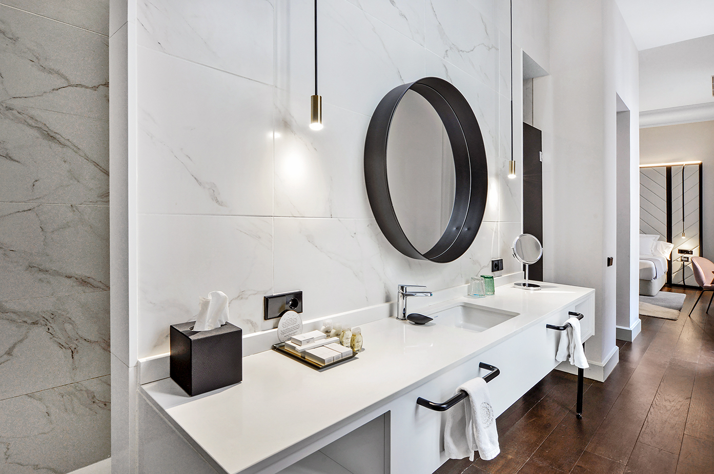 Luxury hotel bathroom vanity, white marble walls, black circular mirror.