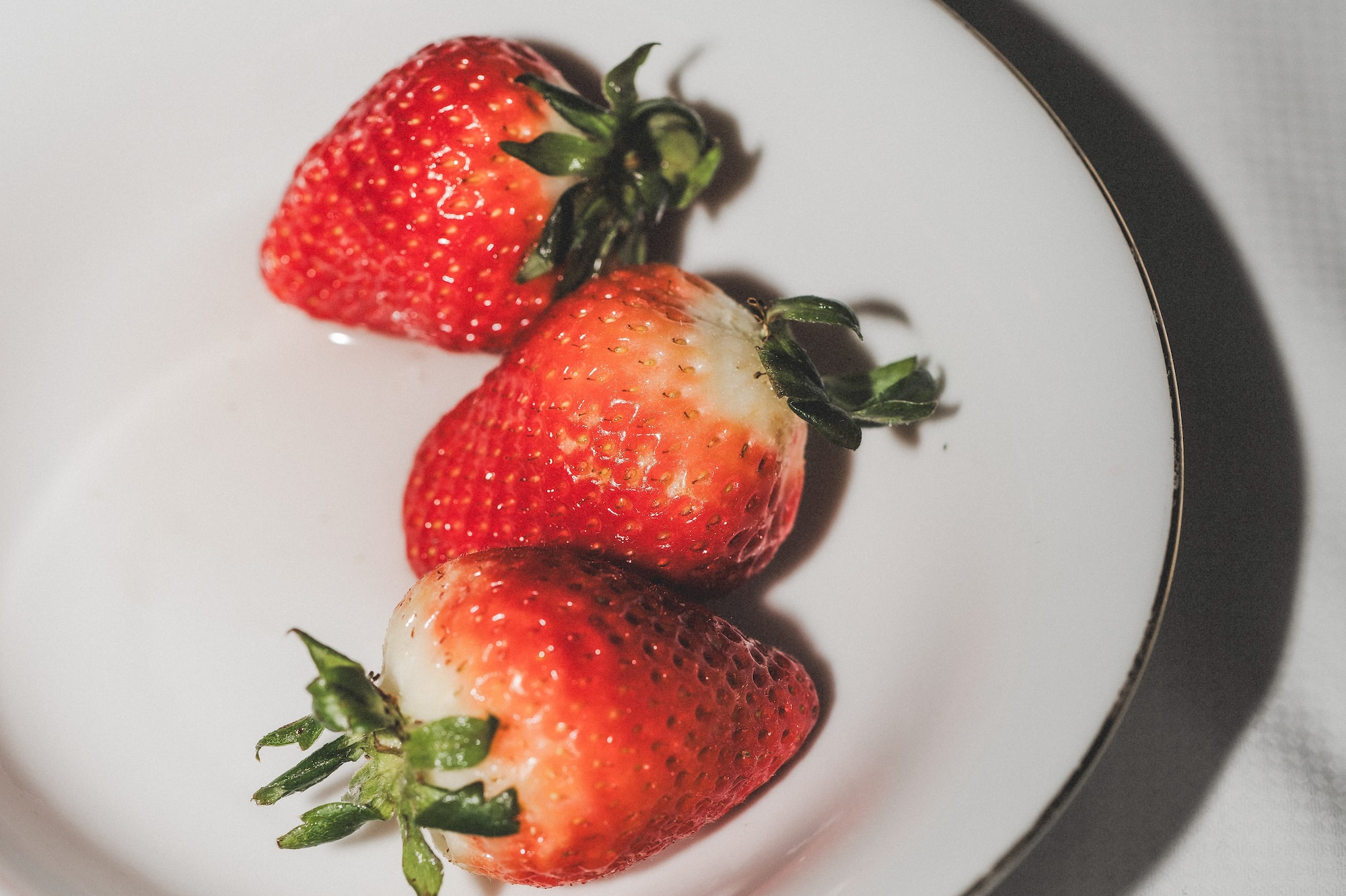 Tres fresas rojas con tallos verdes en plato blanco.