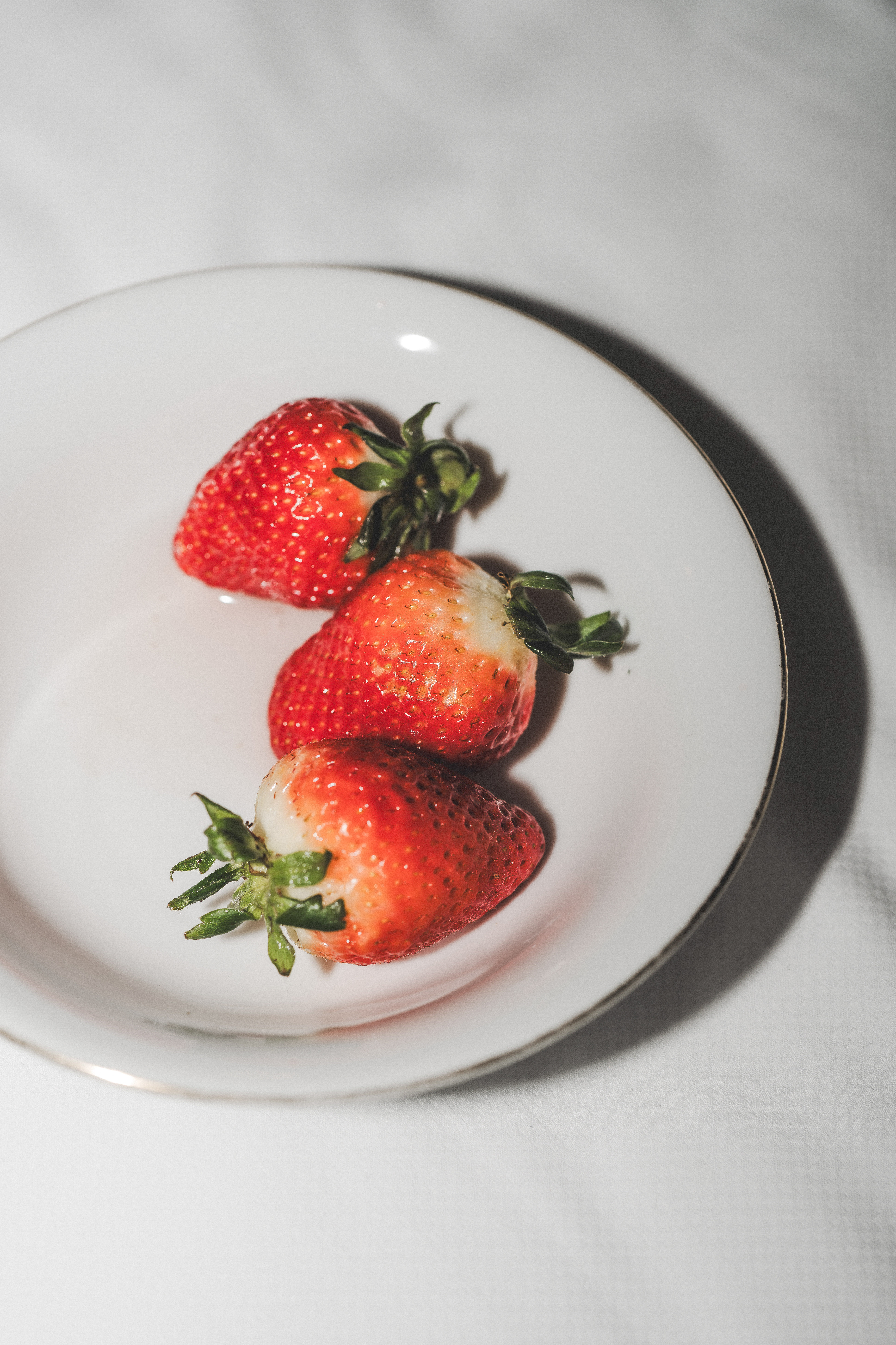 Tres fresas rojas con tallos verdes en plato blanco.