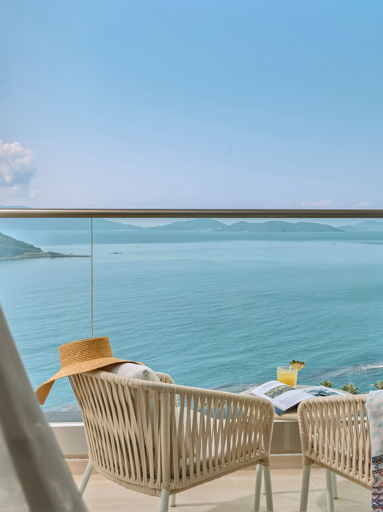 Tropical resort balcony with ocean view, wicker chairs, cocktail, straw hat.