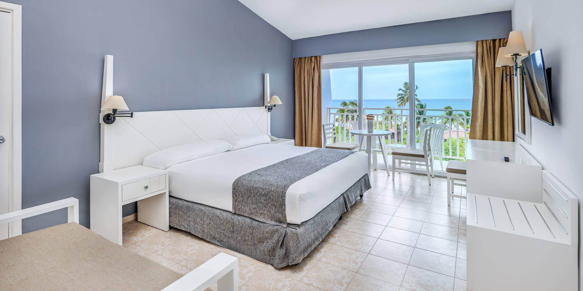 a bedroom with a table and chairs and a balcony overlooking the ocean