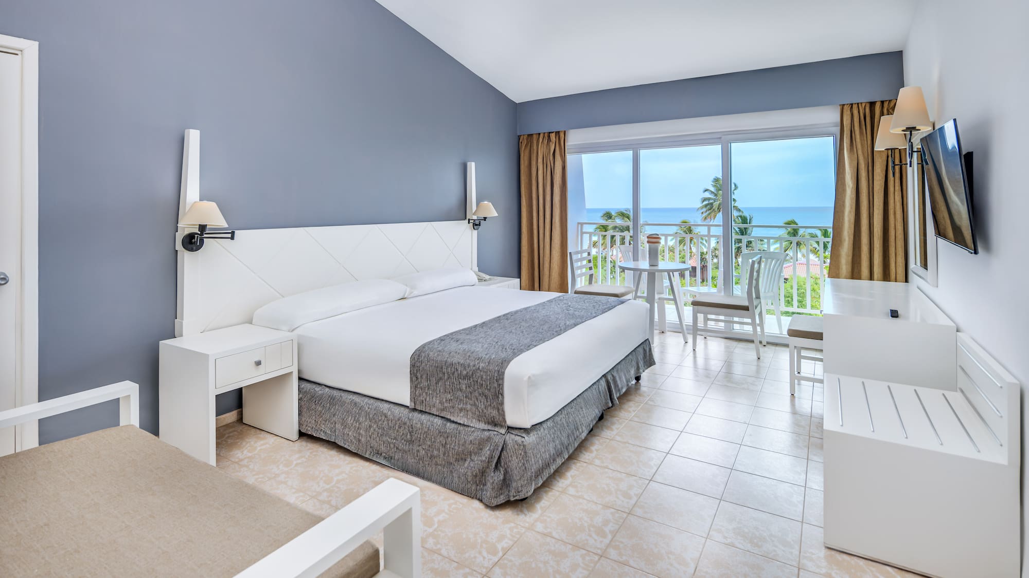 a bedroom with a table and chairs and a balcony overlooking the ocean