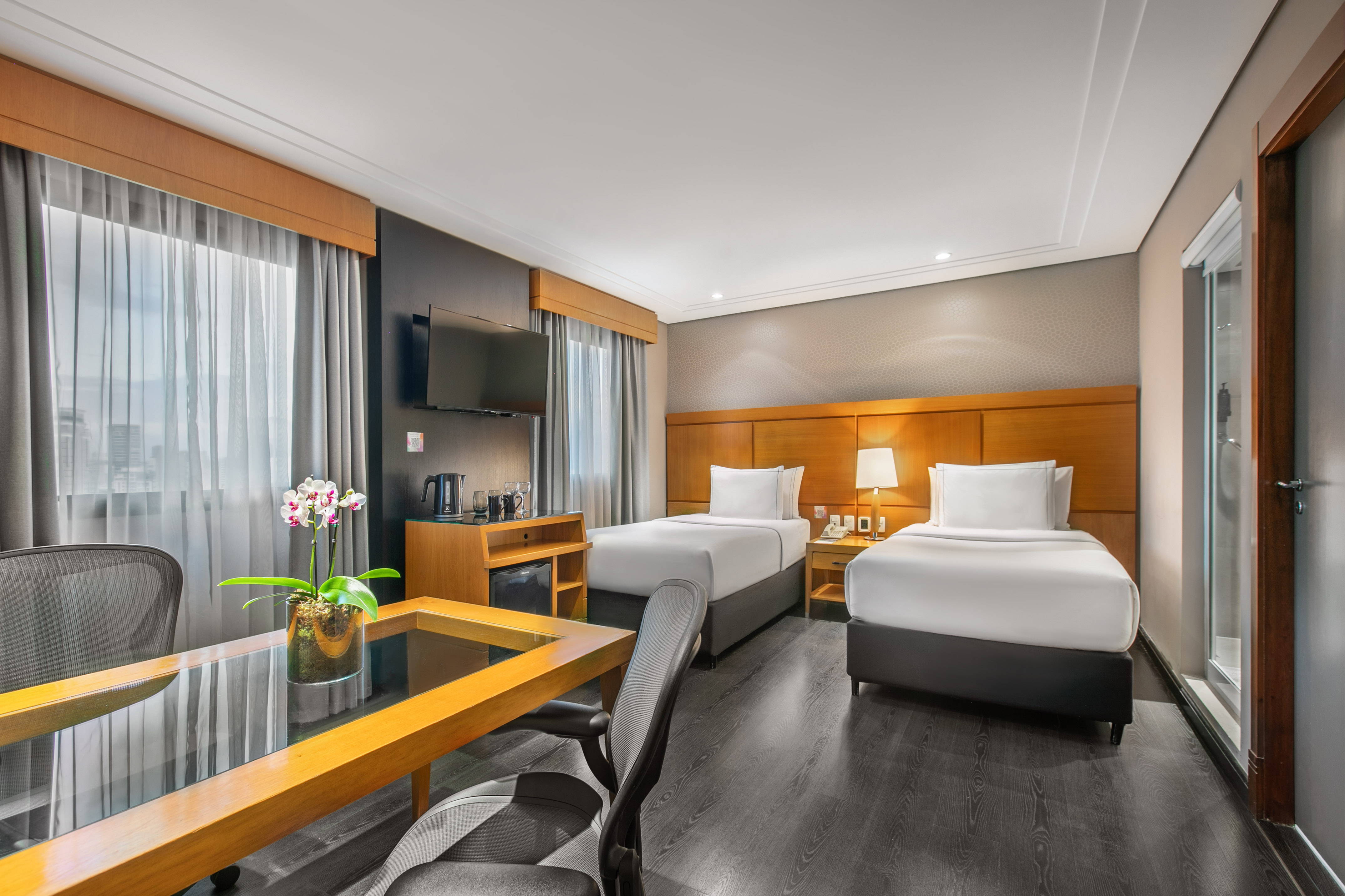 Modern hotel room with two twin beds, work desk, and wall-mounted TV.