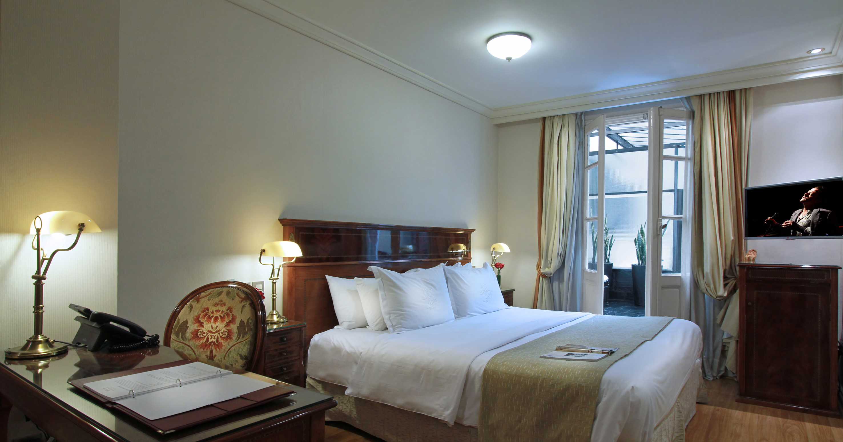 Elegant hotel room with large bed, desk, TV, and balcony doors.