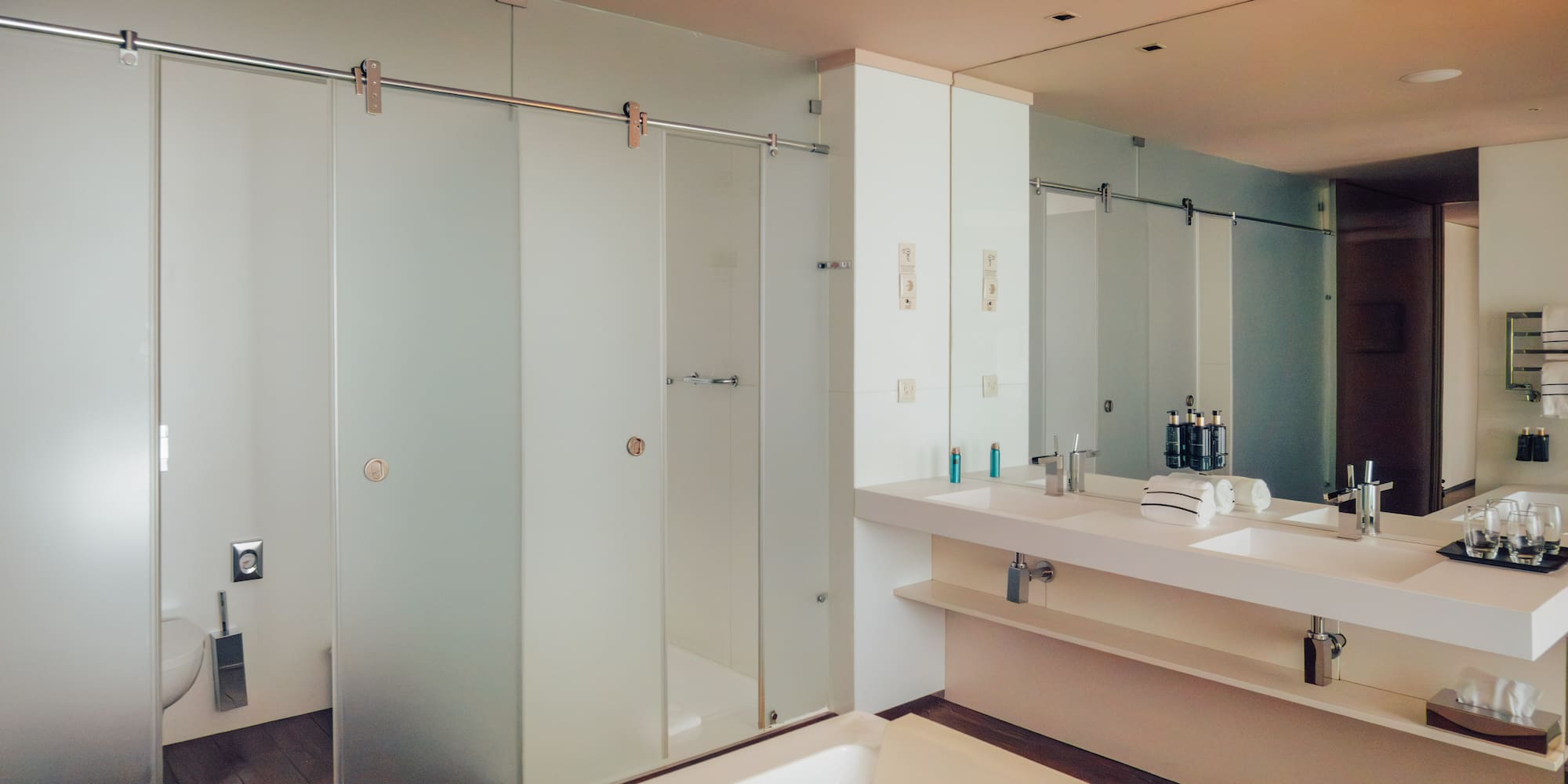 Modern bathroom with white tub, double vanity, and frosted glass shower.