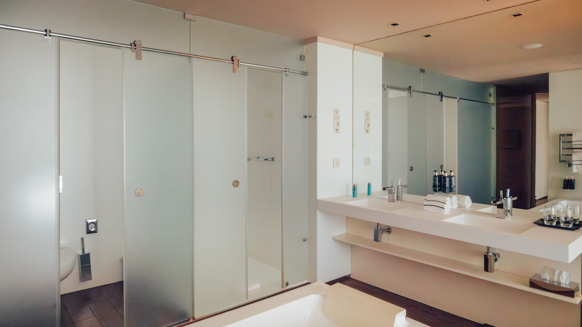 Modern bathroom with white tub, double vanity, and frosted glass shower.