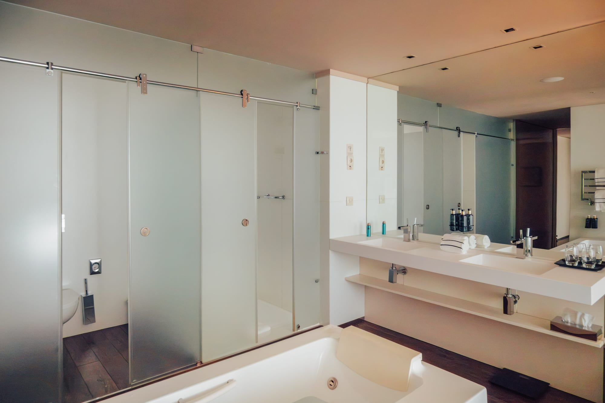 Modern bathroom with white tub, double vanity, and frosted glass shower.