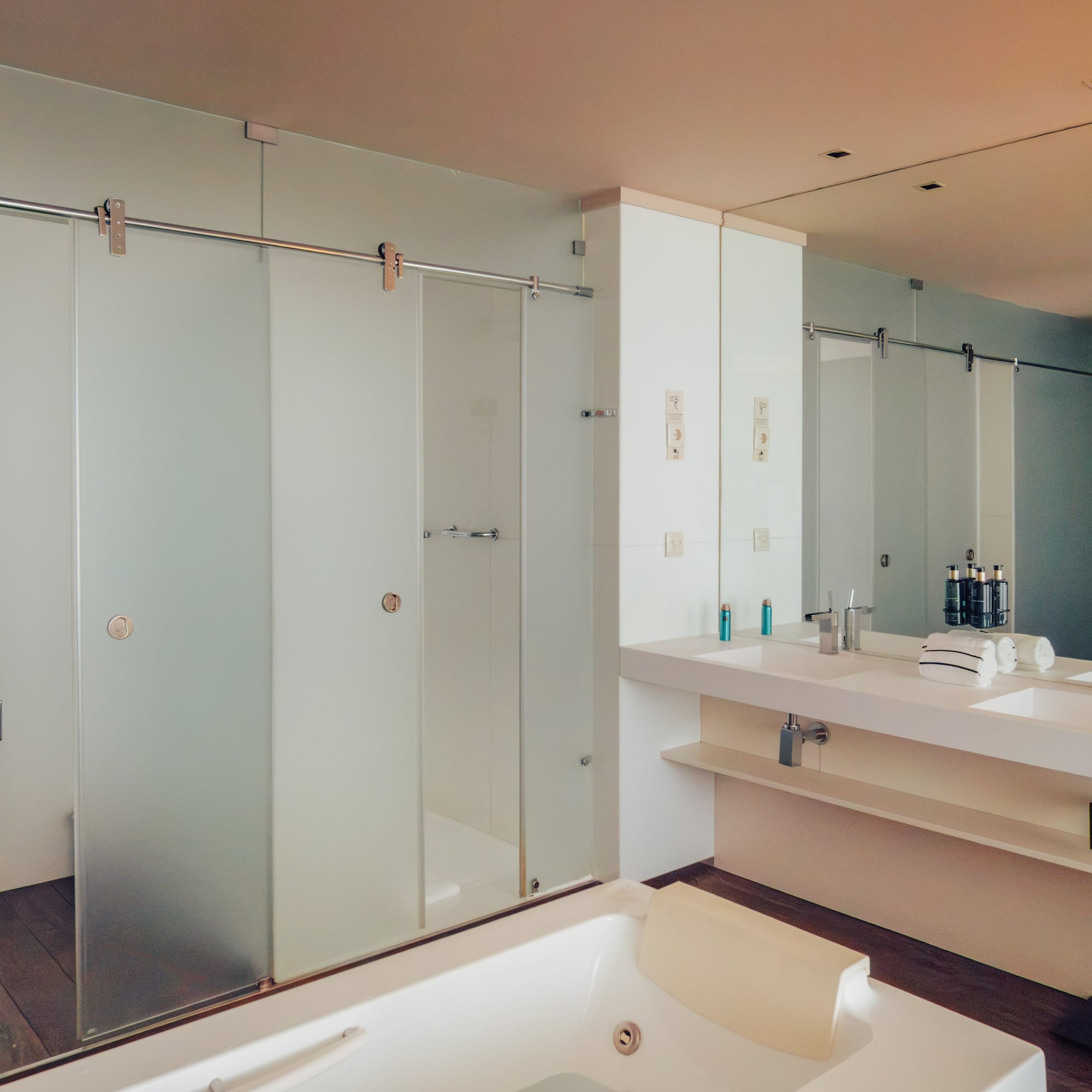 Modern bathroom with white tub, double vanity, and frosted glass shower.