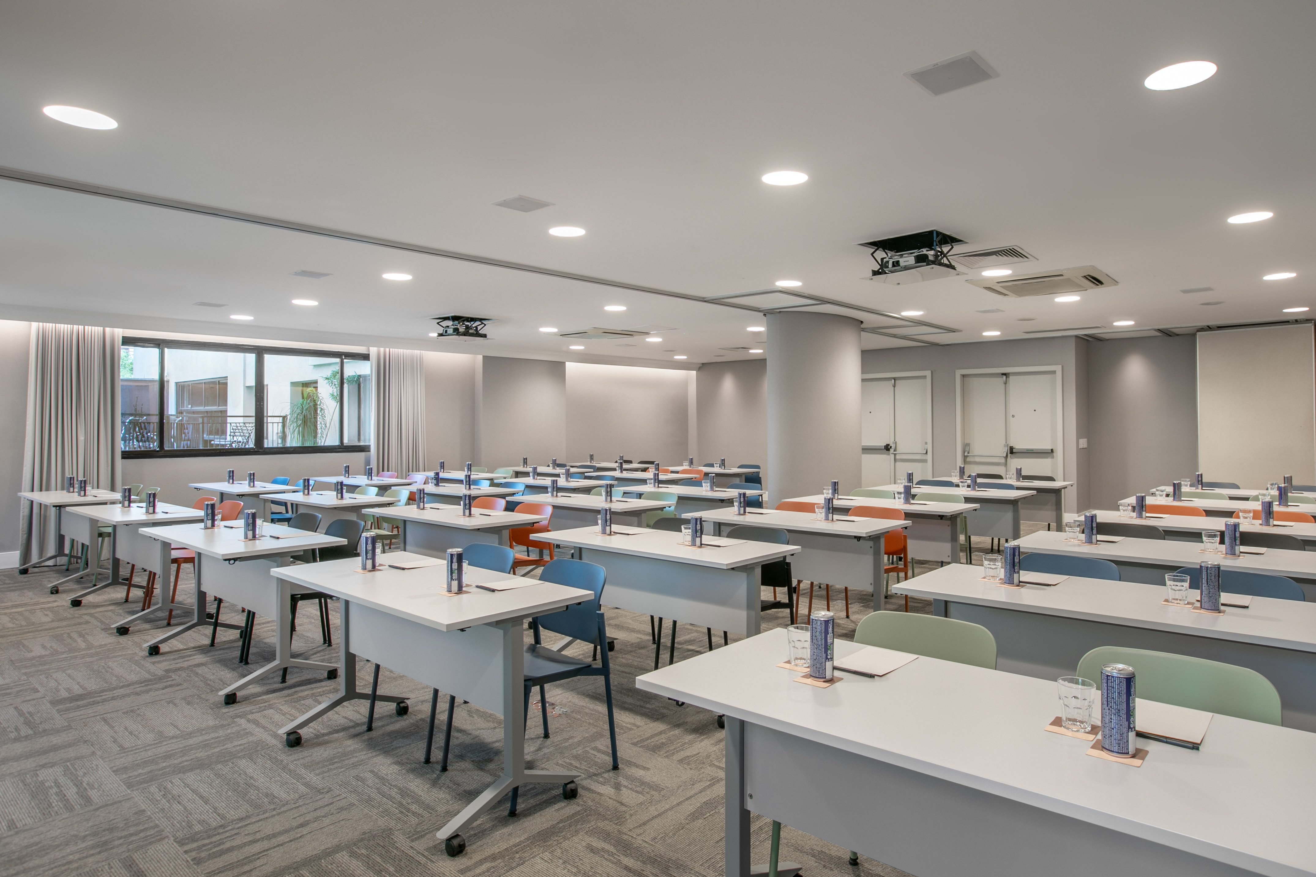 Modern meeting room setup with rows of tables, colorful chairs, and projector.