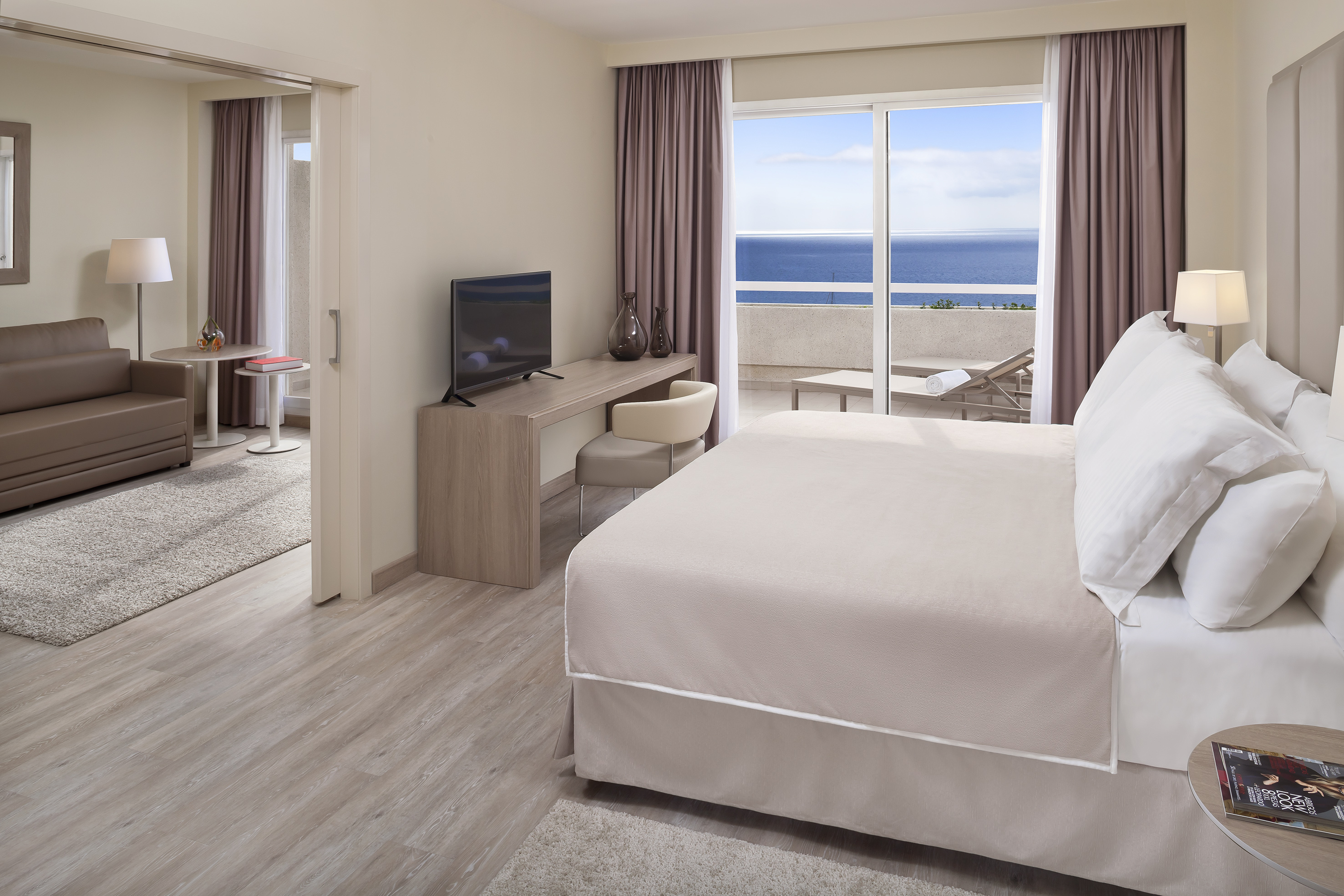 Modern hotel suite with ocean view balcony, king bed, and lounge area.