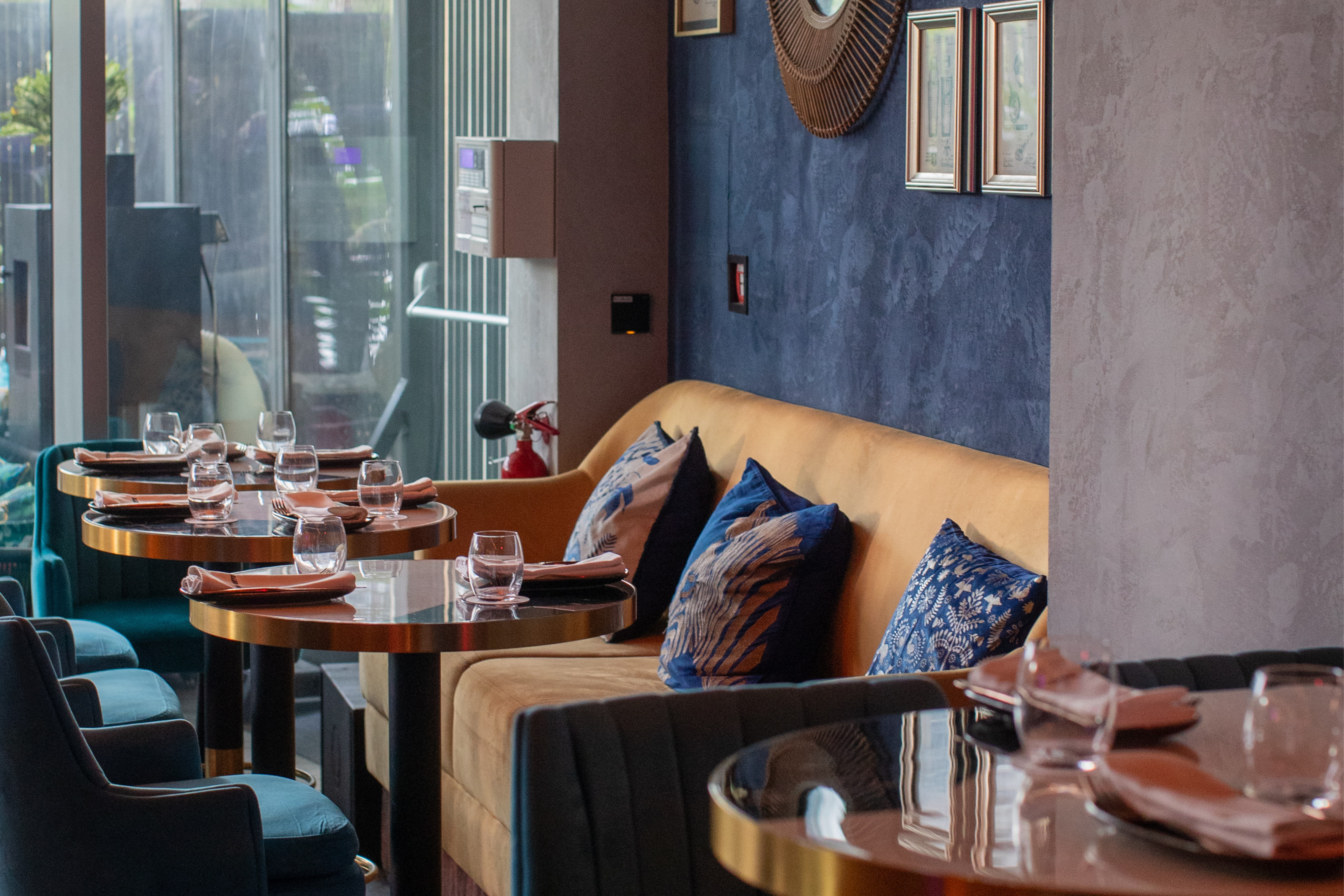 Elegant restaurant interior with gold booth, blue chairs, round tables, and blue wall.
