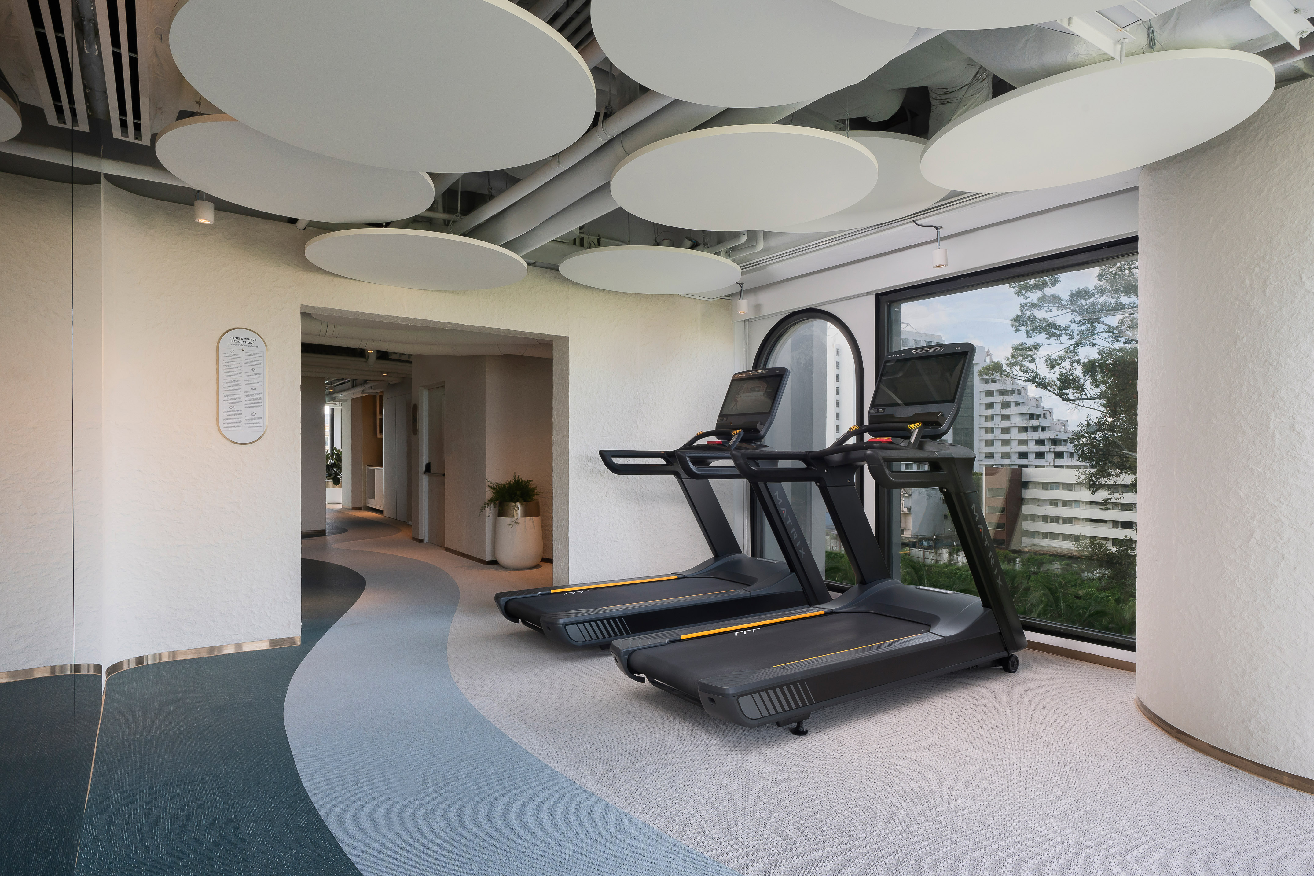 Modern gym interior with two treadmills, circular ceiling, and city view. - Trung tâm thể dục - Meliá Pattaya Hotel, Pattaya