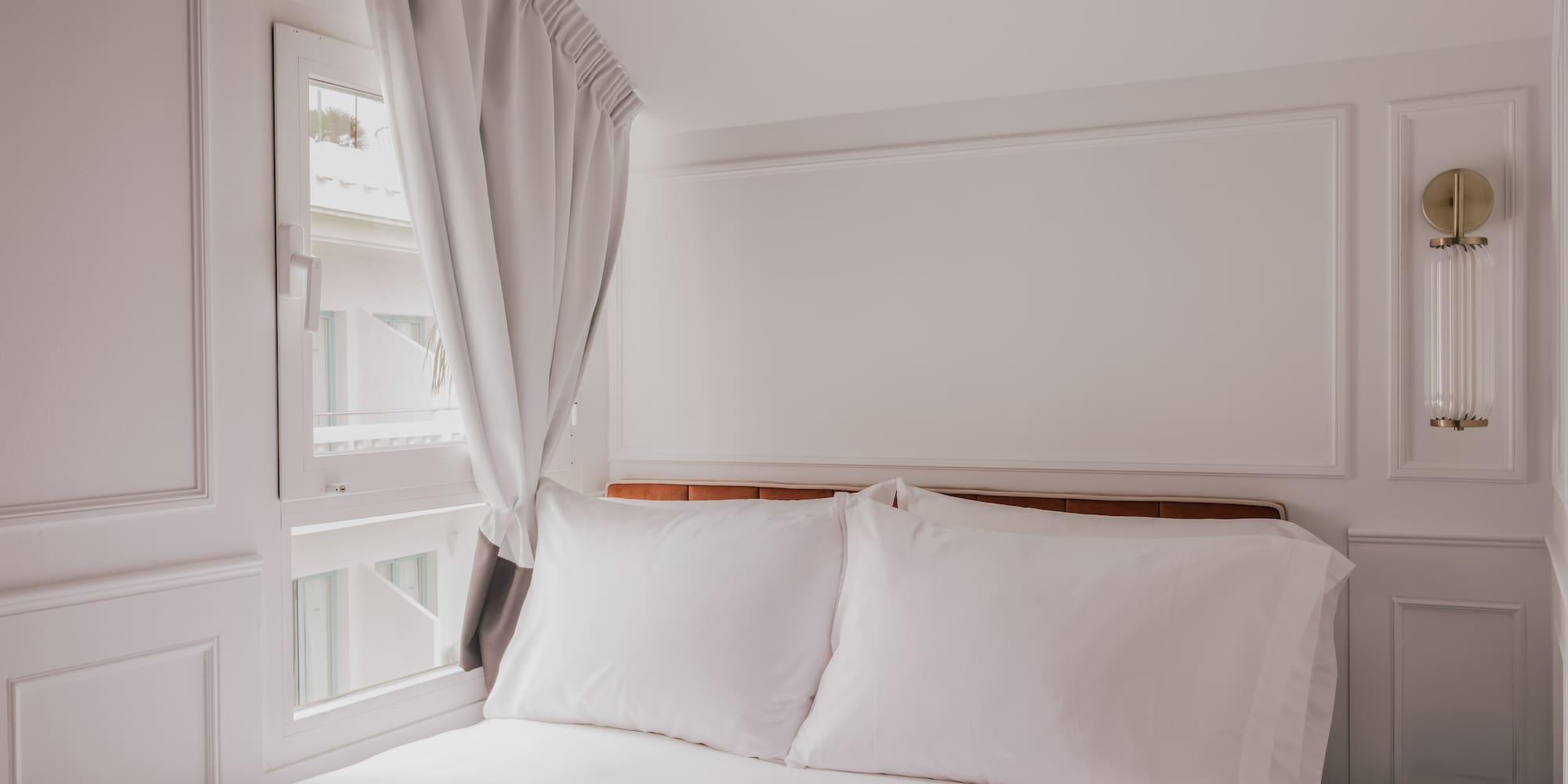 Clean white hotel bedroom with bed, window, nightstand, and vintage phone.