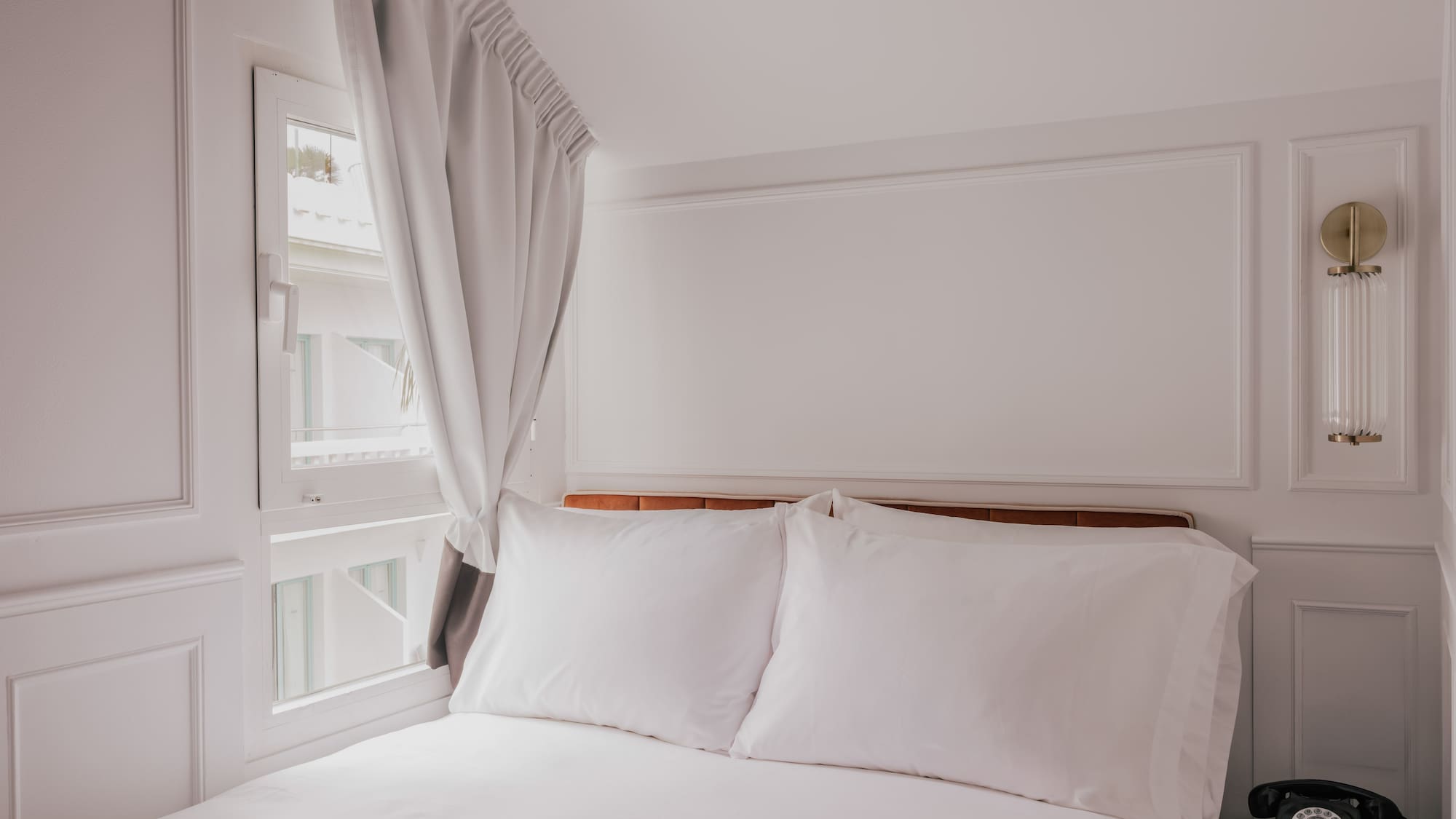 Minimal white bedroom with bed, window, light curtain, and vintage phone.