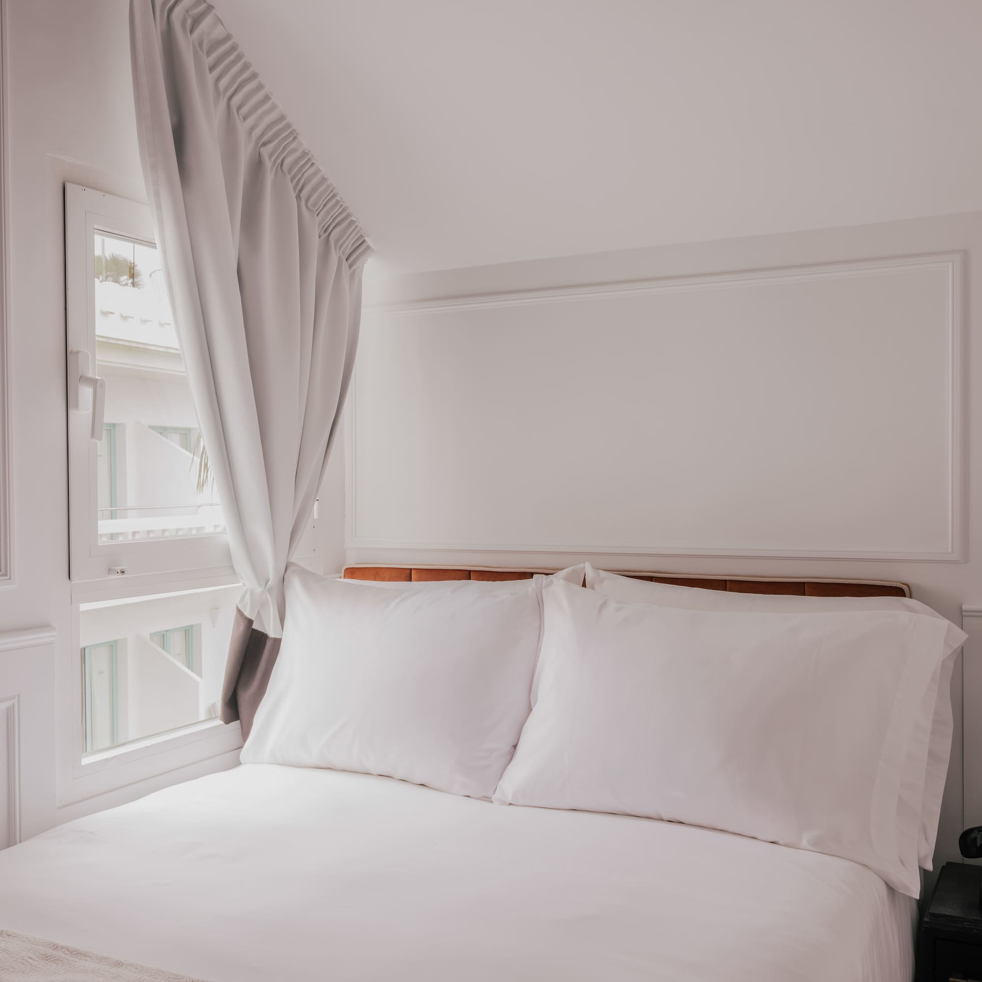 Clean white hotel bedroom with bed, window, nightstand, and vintage phone.