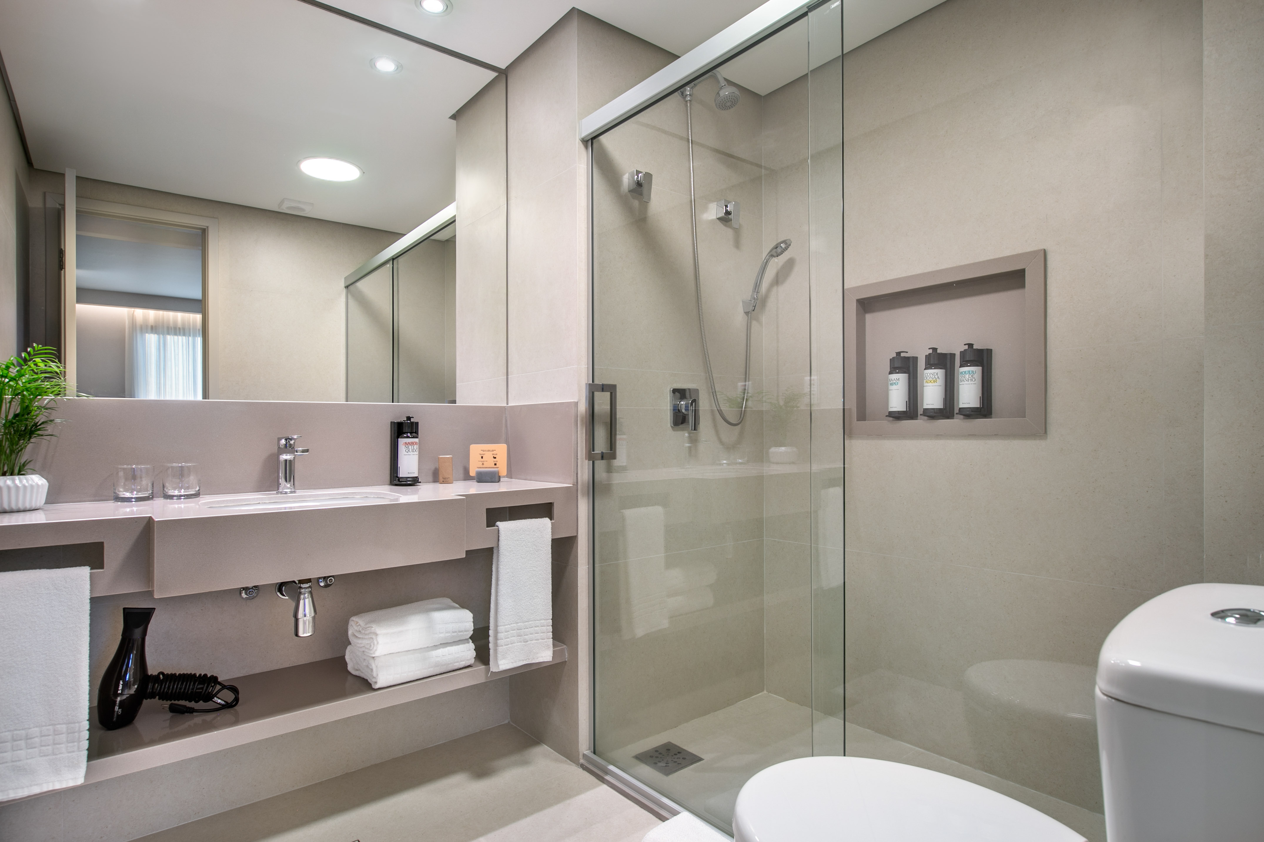 Modern beige bathroom with floating vanity, glass shower, and white toilet.