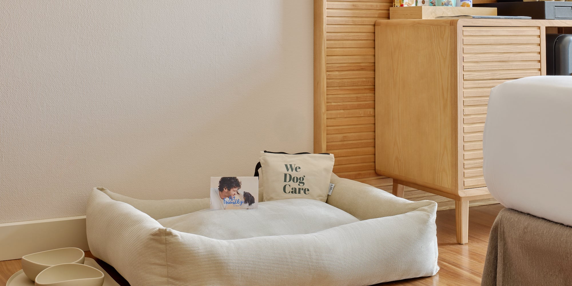 Pet-friendly hotel room: beige dog bed, bowls, and pet care kit.