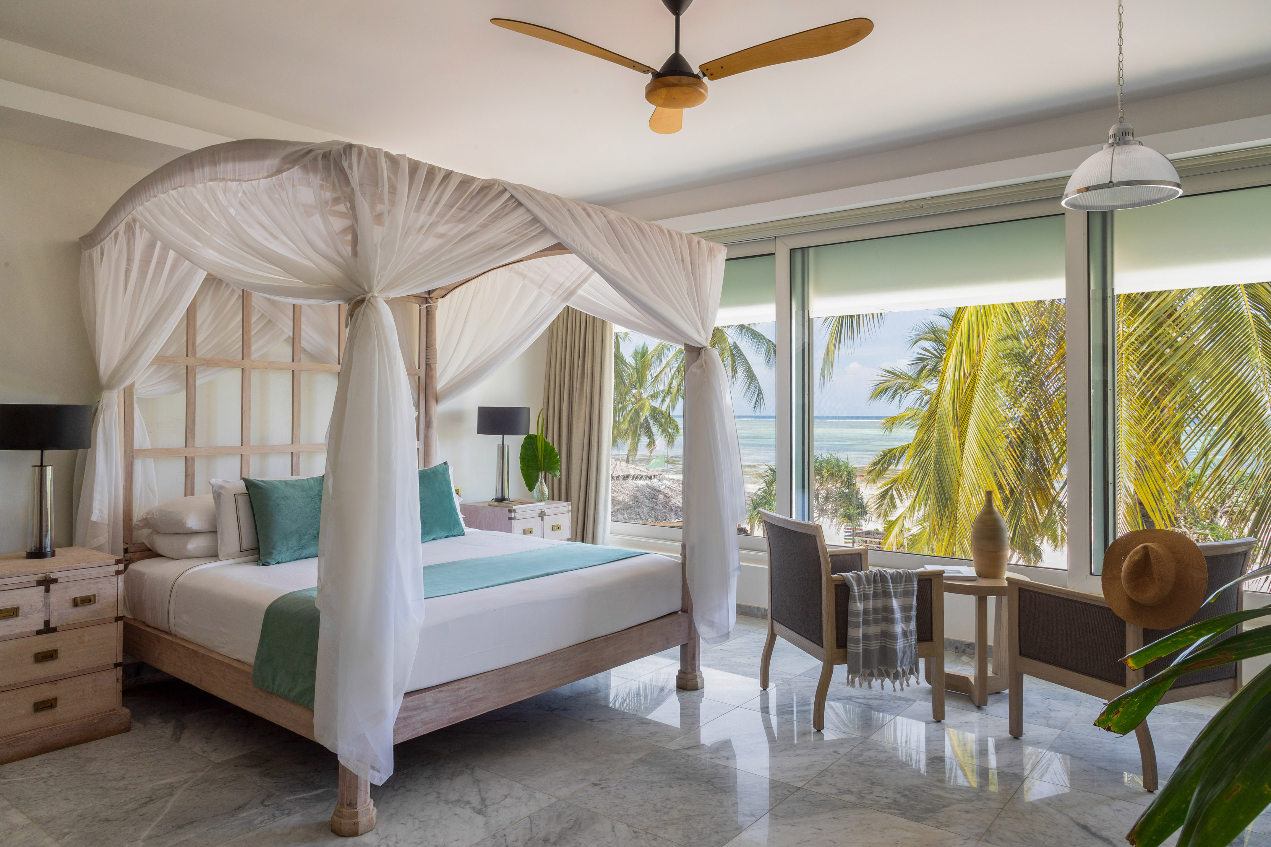 Luxury resort room with four-poster bed, ocean view, and palm trees.