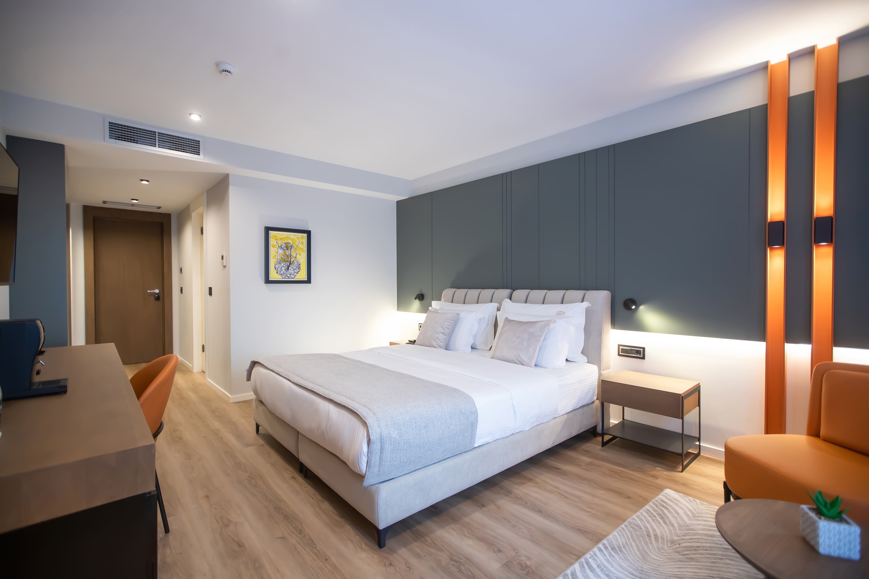 Modern hotel room with cozy bed, grey accent wall, orange panels, and wood floor.