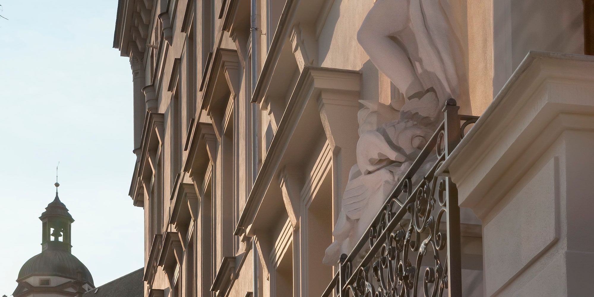 Historic building facade with statue playing horn on ornate balcony, church tower.