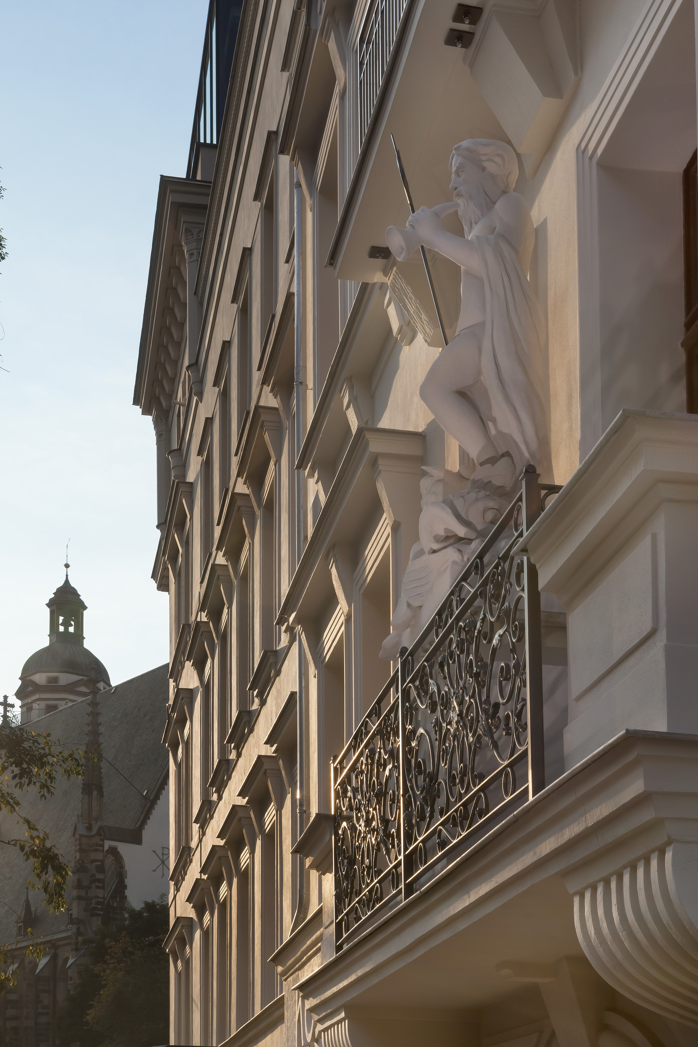 Historic building facade with statue playing horn on ornate balcony, church tower.