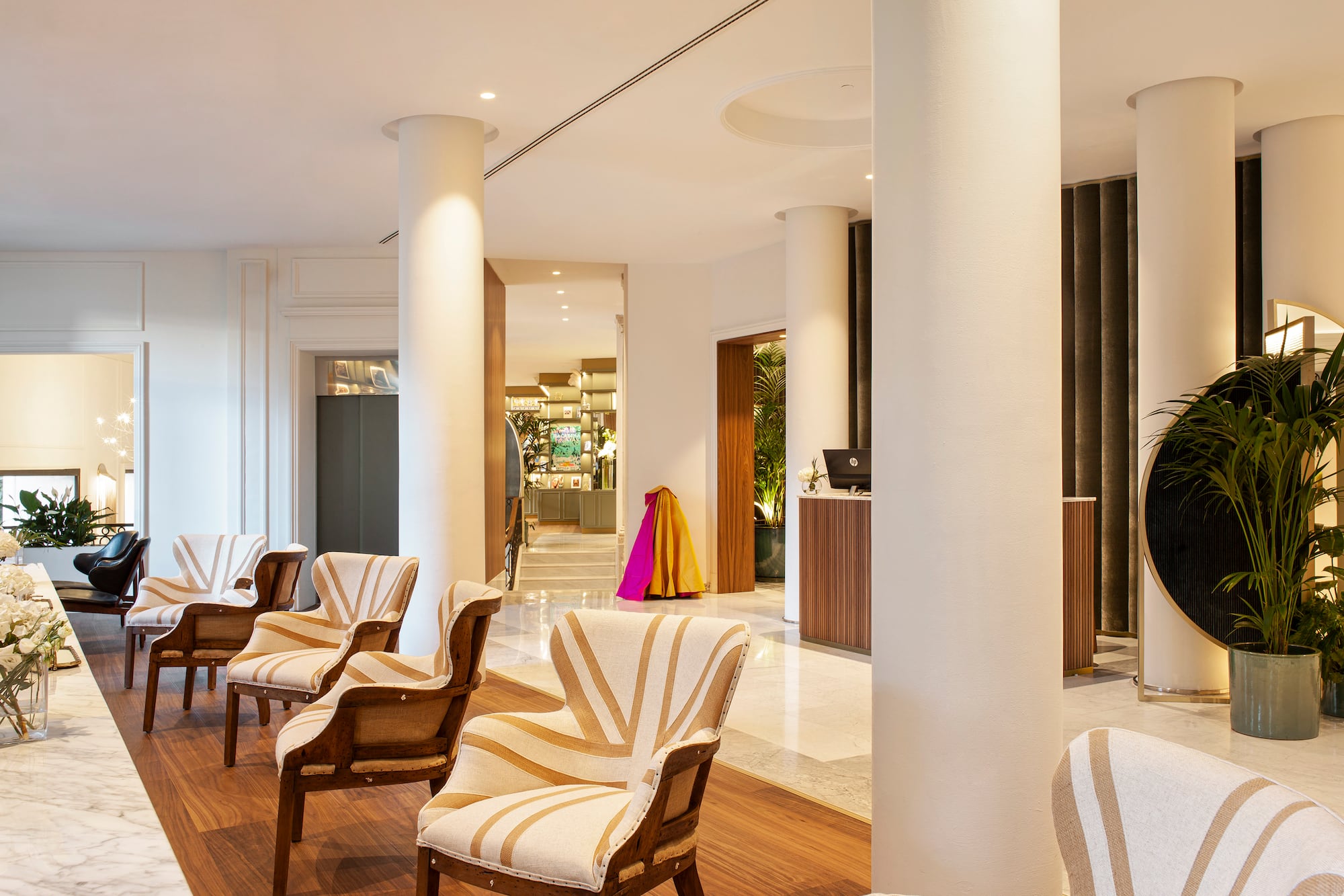Hotel lobby with striped lounge chairs, white columns, and reception area.